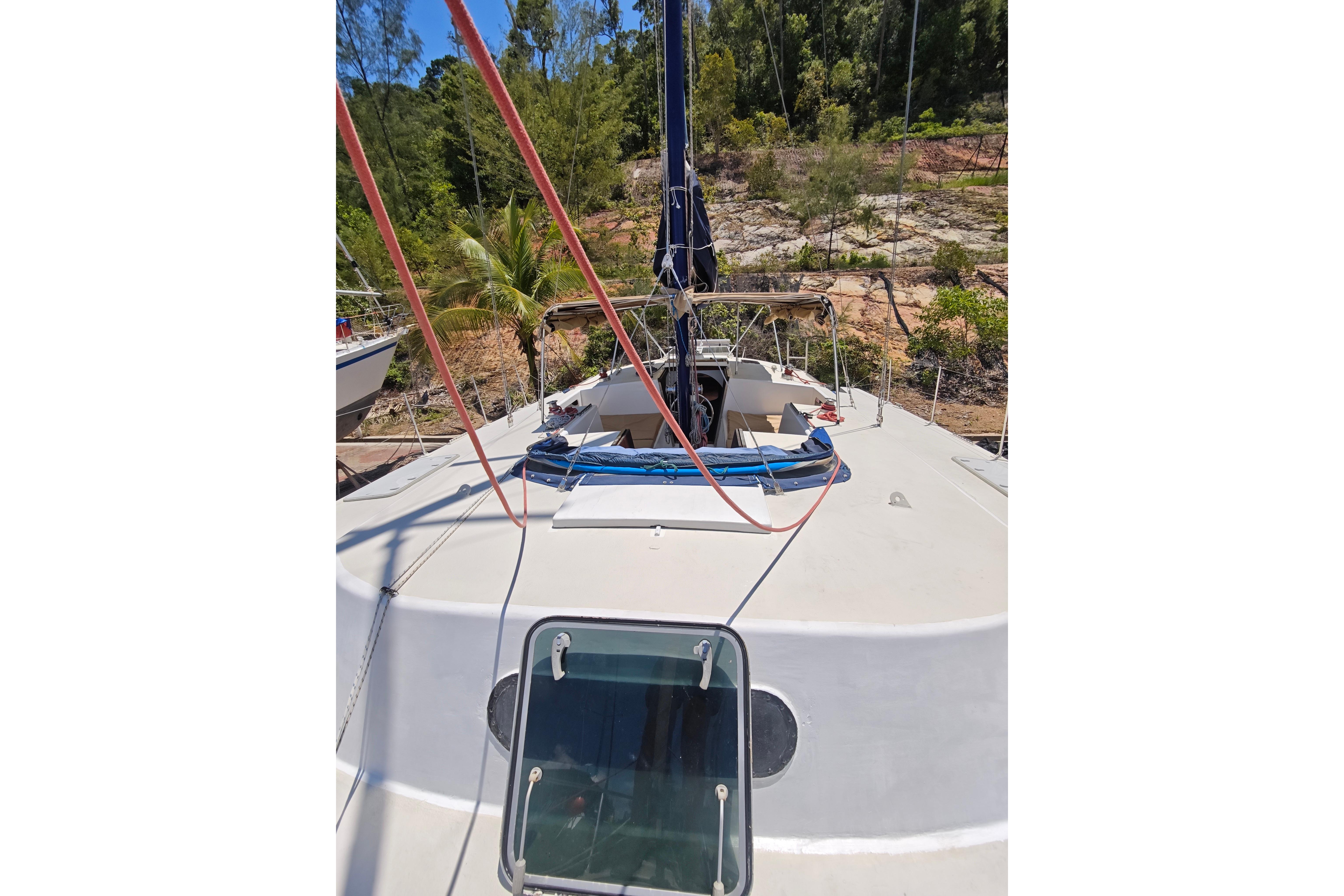1979 Searunner 37 sailboat deck with ropes, hatch, and lush greenery background.