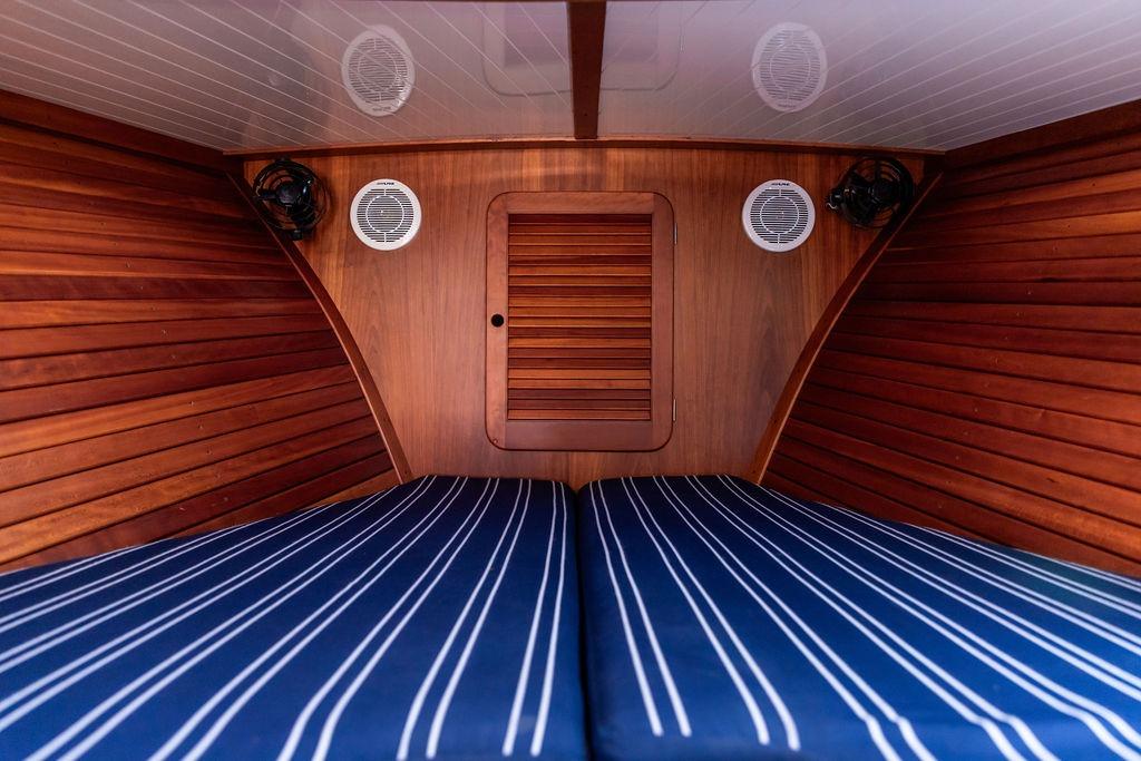 Interior cabin of 2000 Hinckley Picnic Boat 36 Classic with striped bedding and wooden paneling.