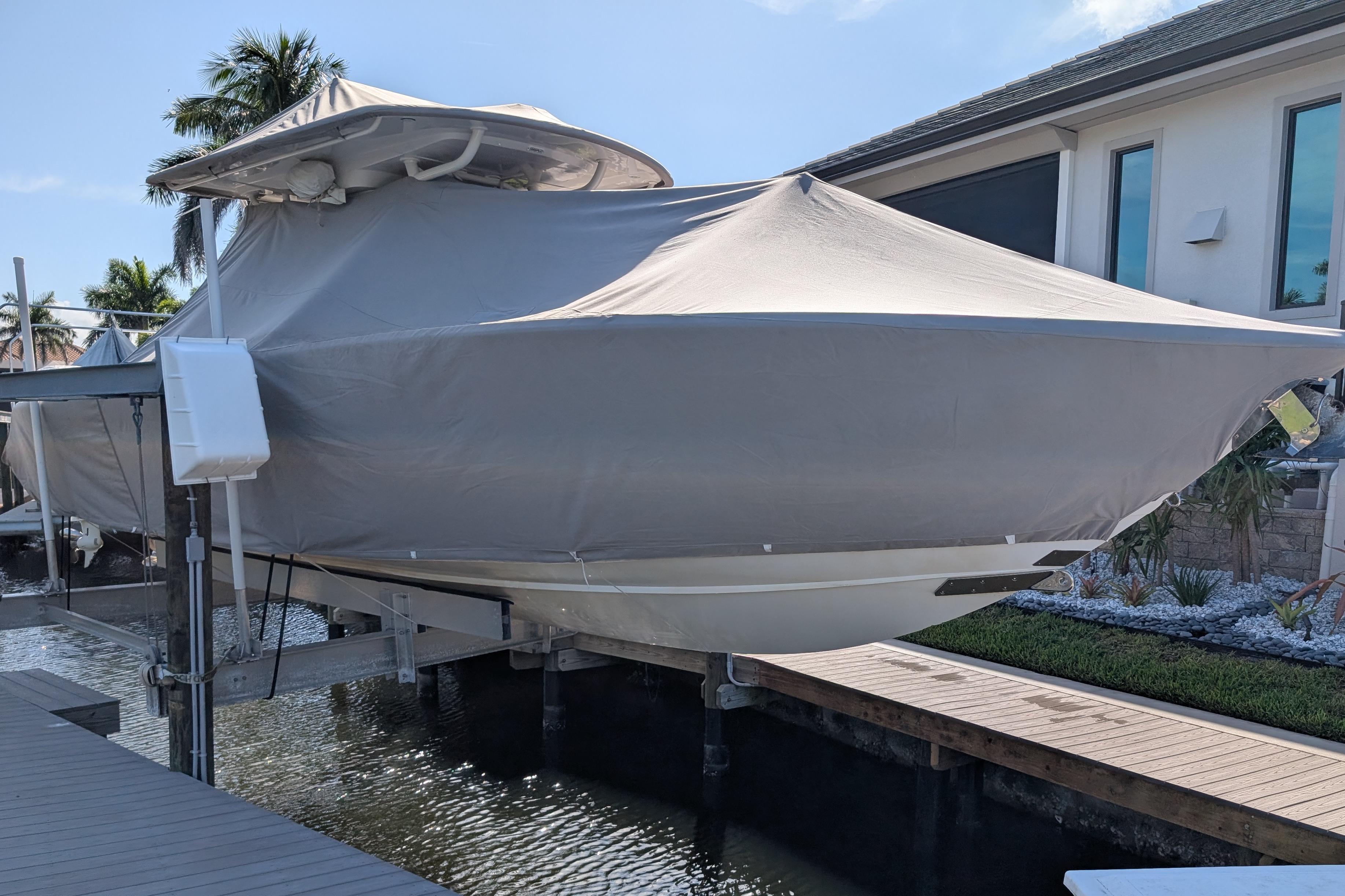2015 Jupiter 34 HFS boat covered and docked near a waterfront home.