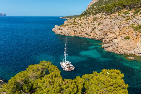 Sailing yacht Lagoon 60 (2025) anchored in a scenic, rocky coastal bay.