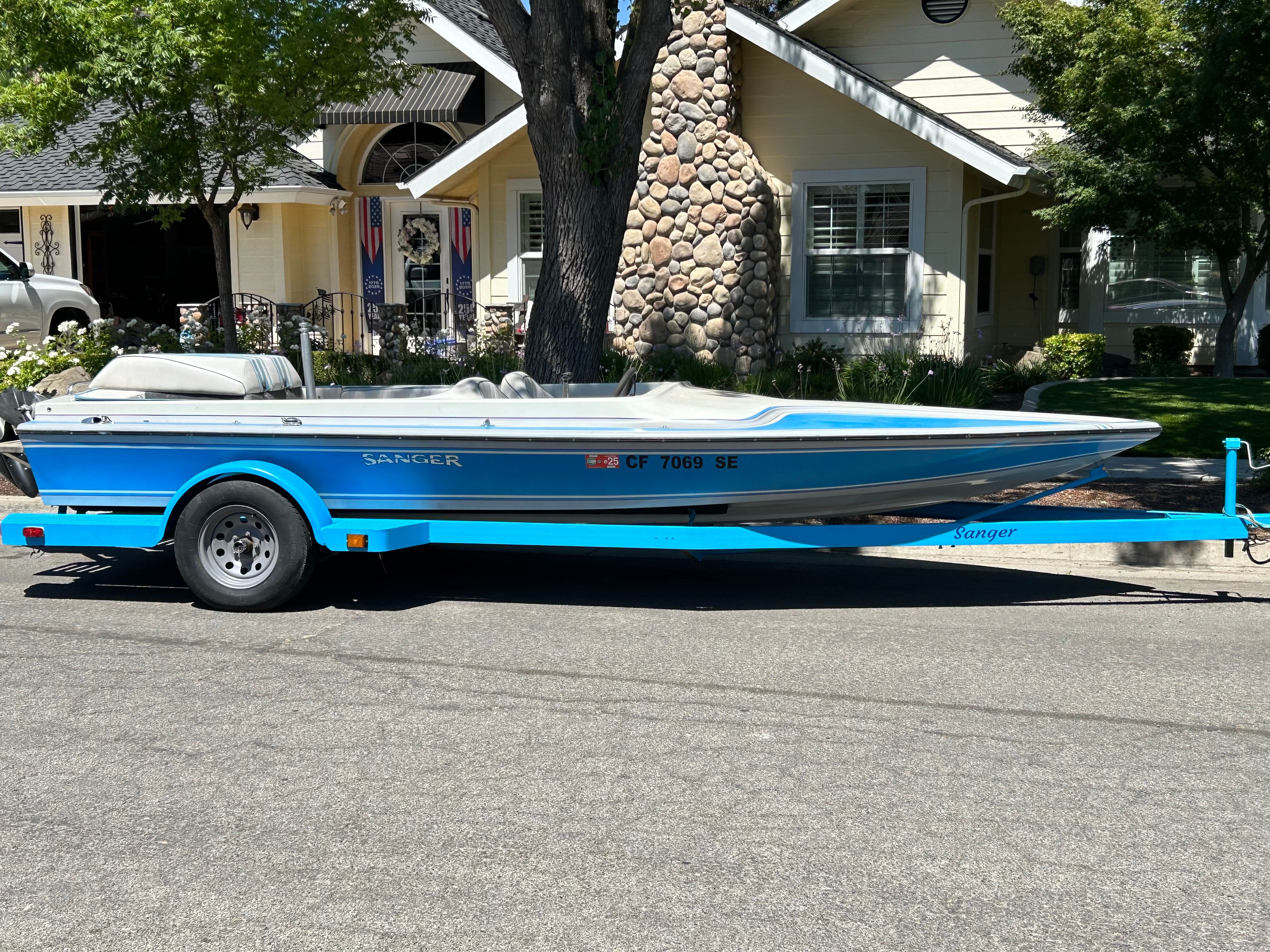 A blue 1988 Sanger Ski Tug on a trailer, parked on a street in front of a house.