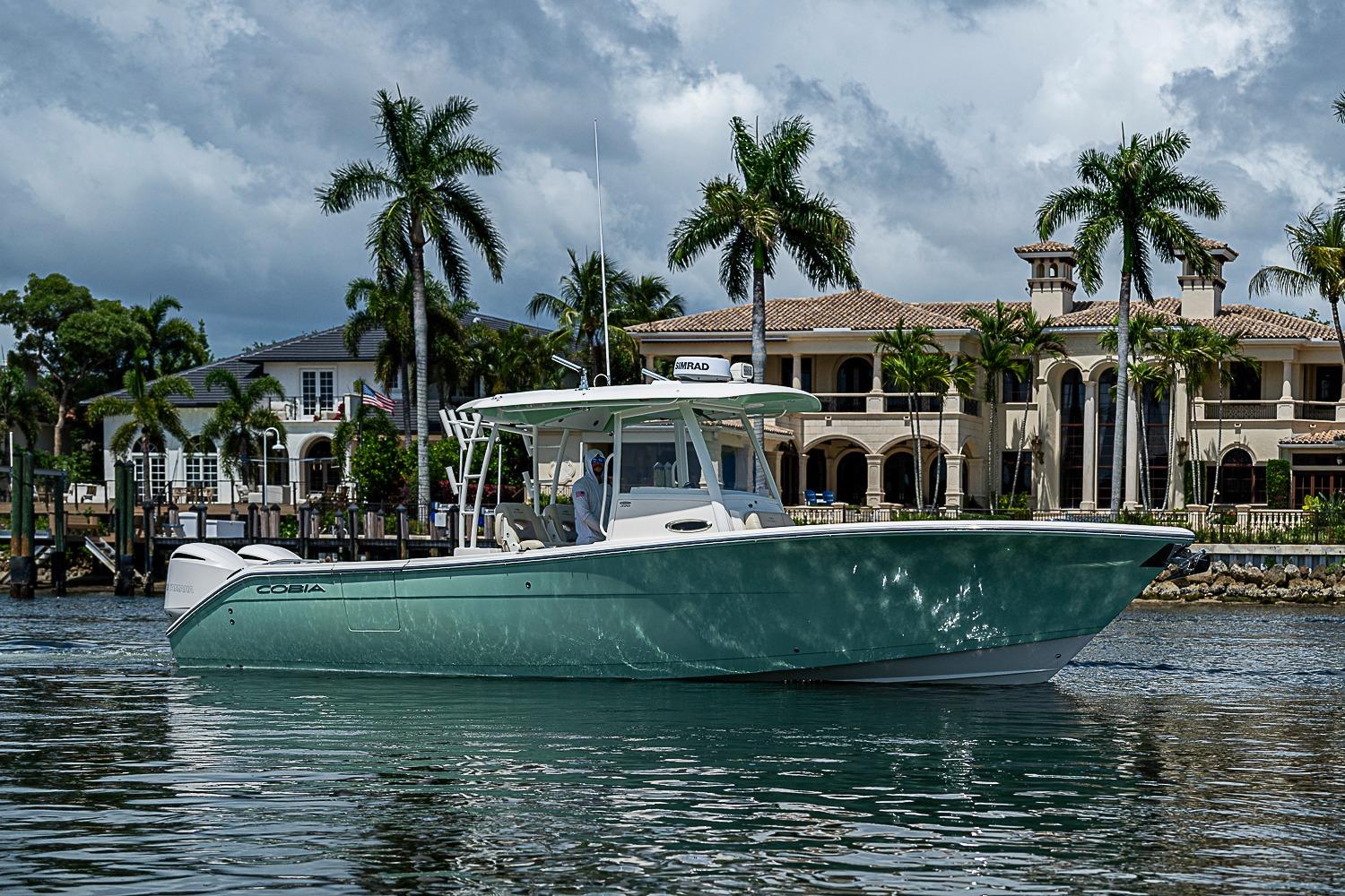 2019 Cobia 320 Center Console boat on water, with luxury homes and palm trees in background.