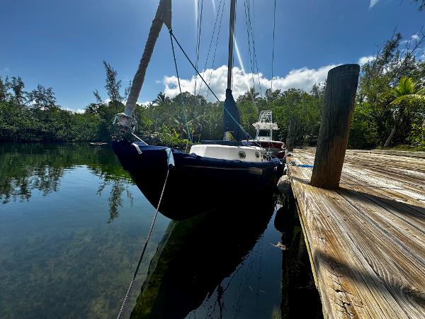Vintage 1968 Sailboat 24 docked on calm water, surrounded by lush greenery.