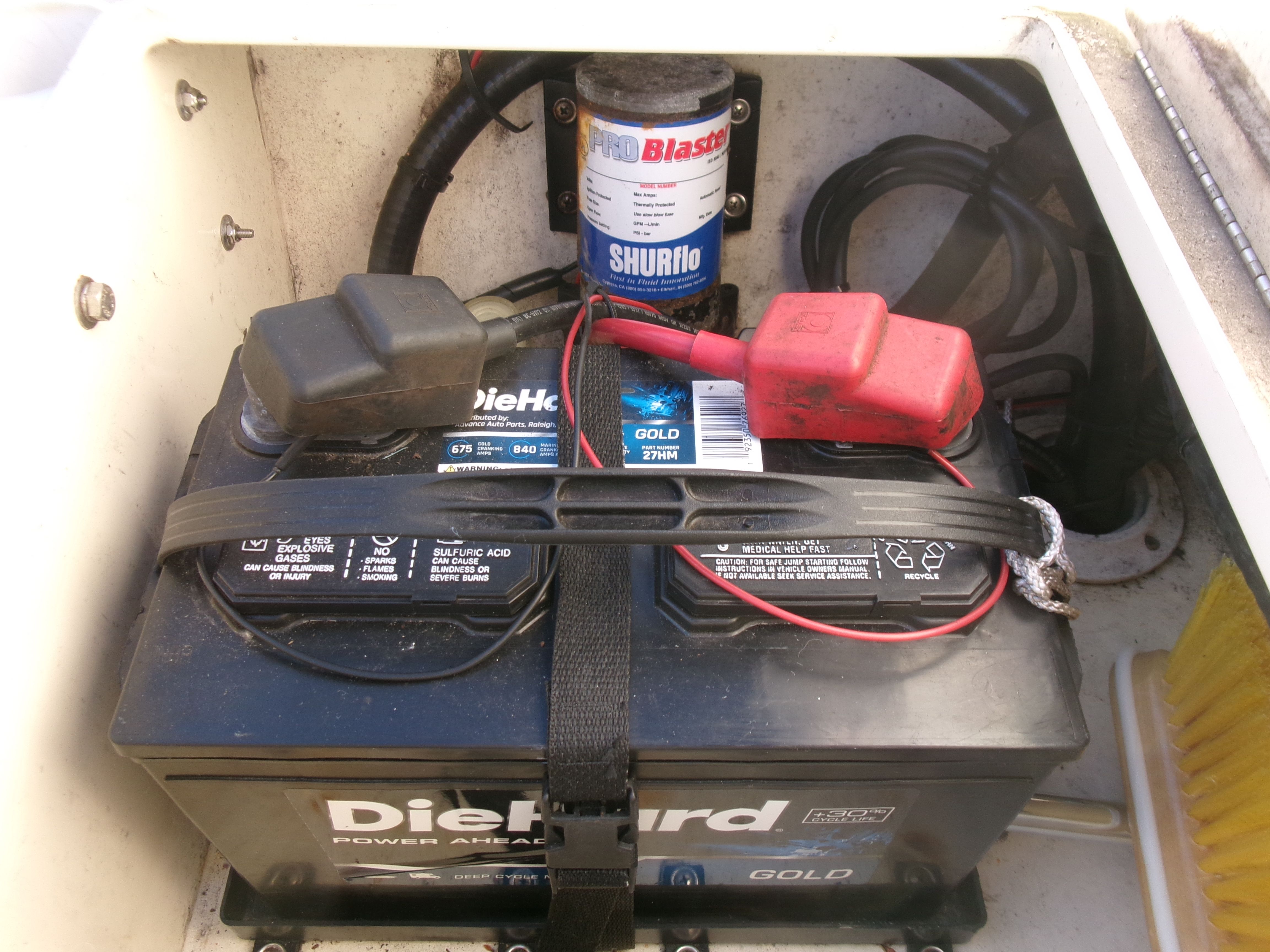 Battery and filter in a boat engine compartment, with cables and a securing strap.