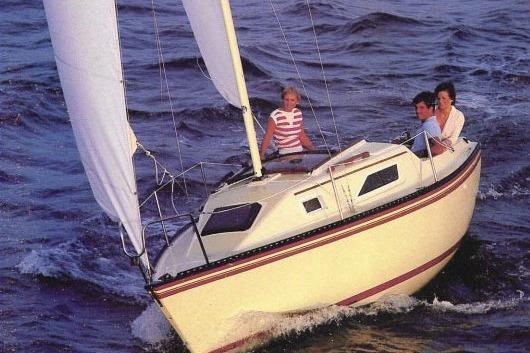 1984 Hunter 22 sailboat navigating ocean waves with three people onboard.