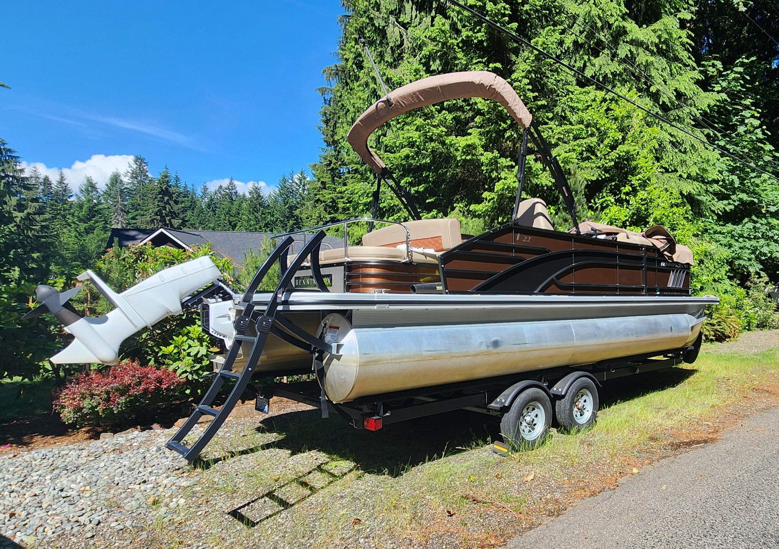 A 2023 Bennington 22 LSB pontoon boat on a trailer, surrounded by trees and clear skies.