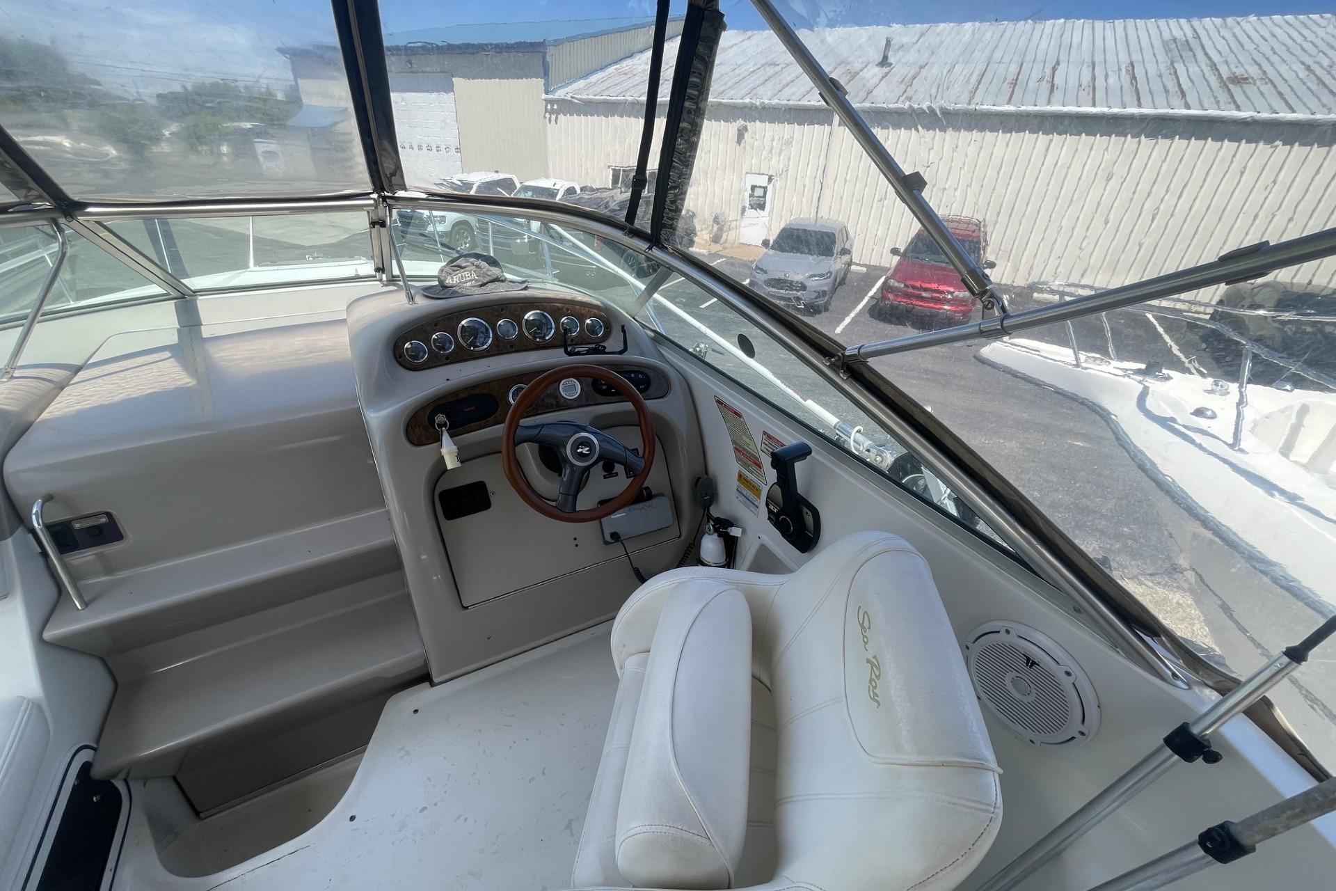 Cockpit of 2000 Sea Ray Sundancer 260 with steering wheel and gauges, docked near vehicles.