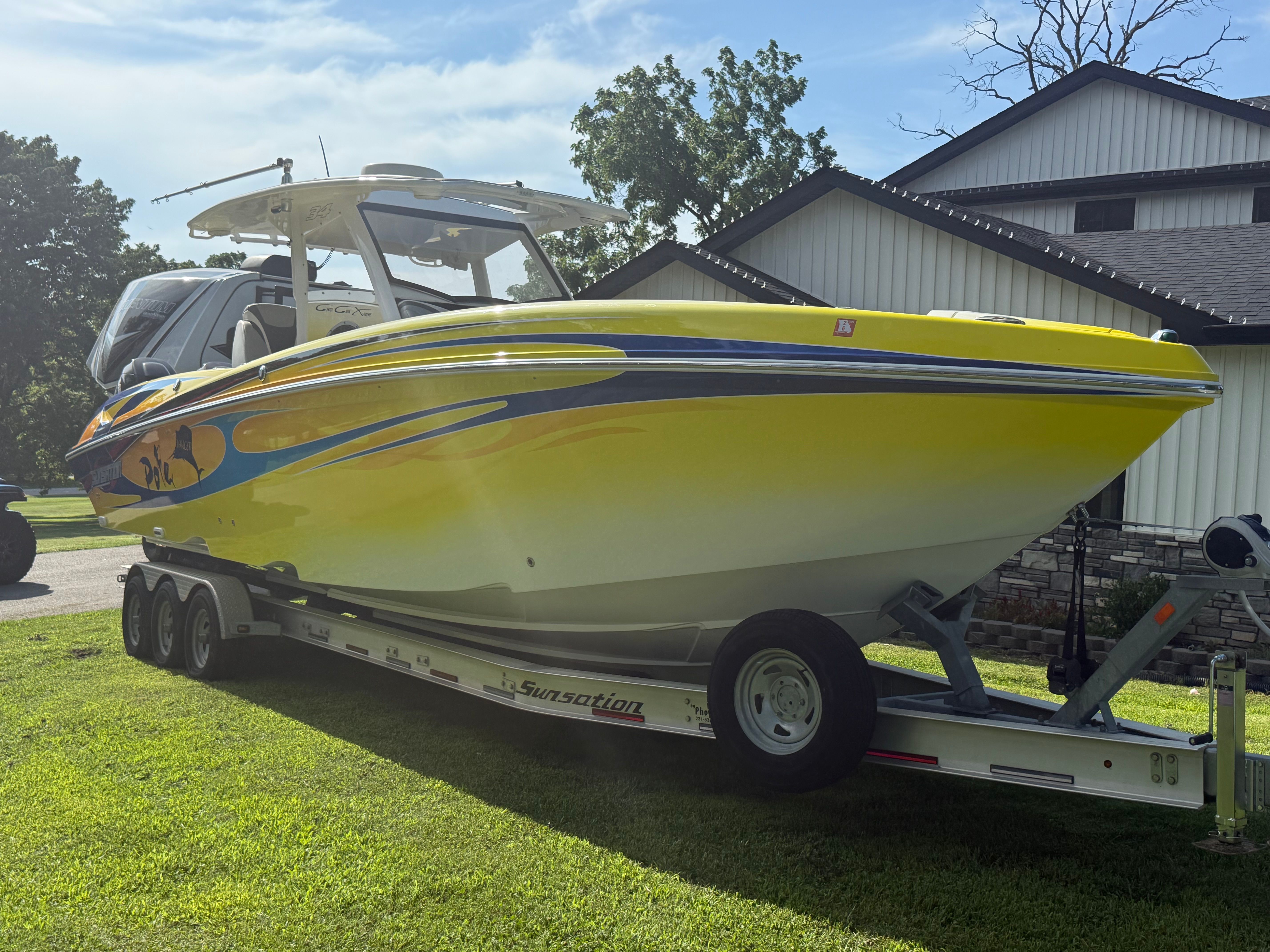 A yellow boat on a trailer on the grass, with a house in the background.