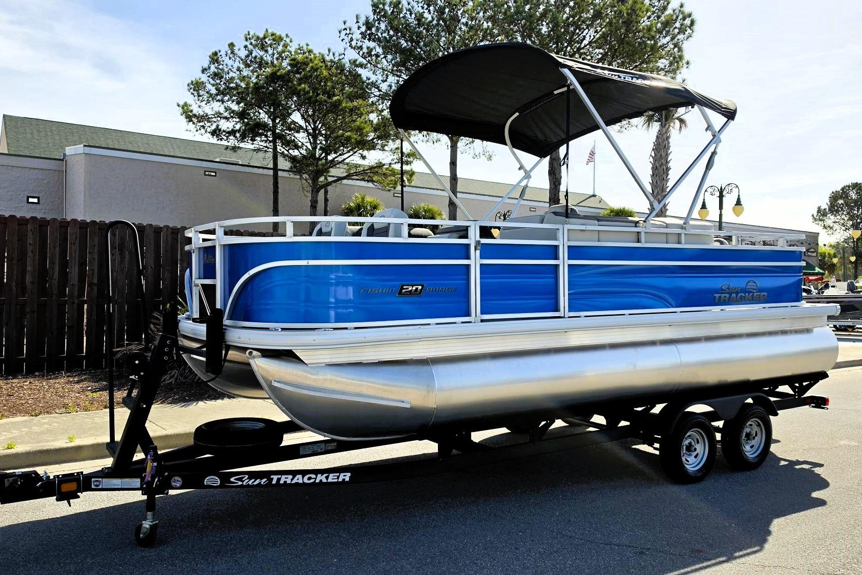 2026 Sun Tracker Fishin' Barge 20 DLX pontoon boat on trailer, blue and silver design.