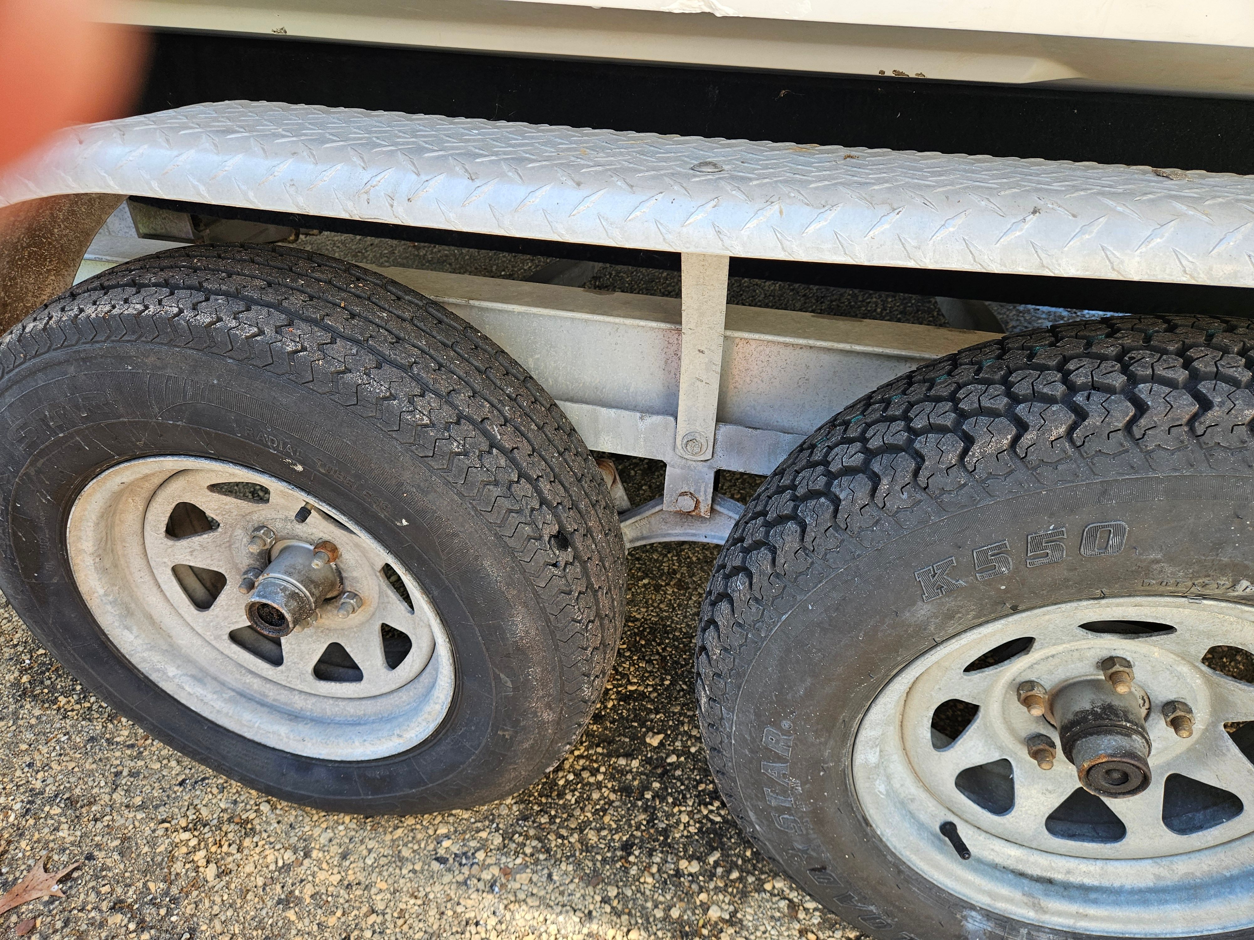 Close-up of a boat trailer with two tires on a gravel surface.