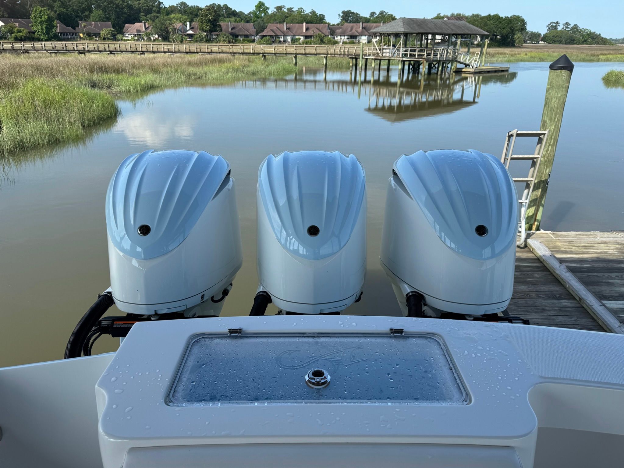 Three outboard engines on a boat docked by a calm river with a pier.
