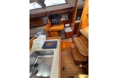 Interior of 1986 Beneteau First 305 sailboat with wooden cabinetry and compact kitchen area.
