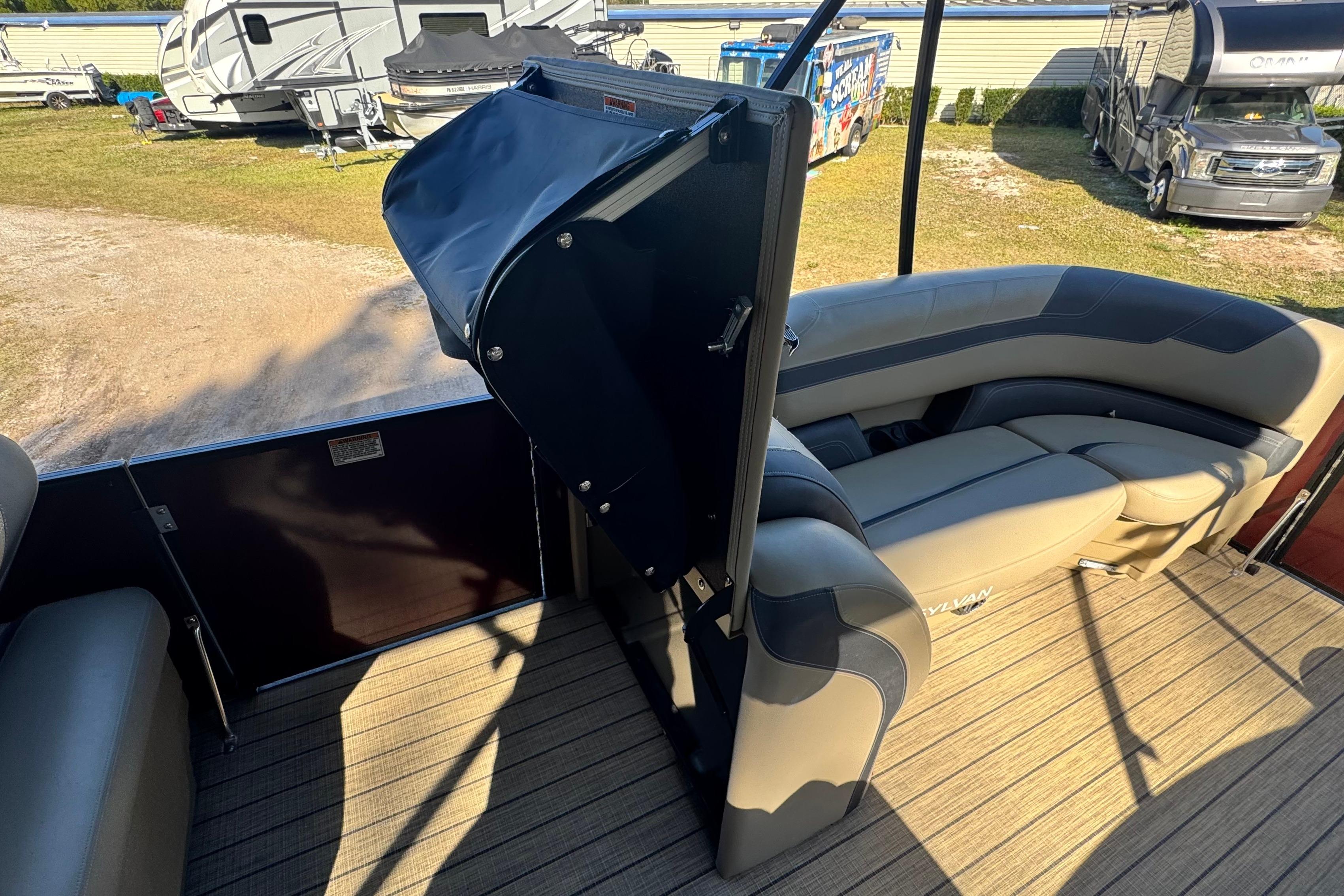 2023 Sylvan L5 CLZ boat interior with seating and storage, parked near RVs.