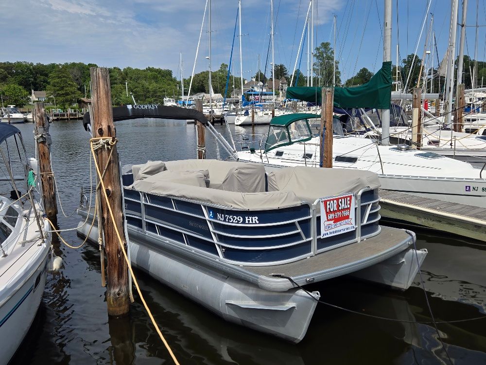 A 2022 Godfrey Sweetwater 2186C pontoon boat docked in a marina, covered with a tarp.