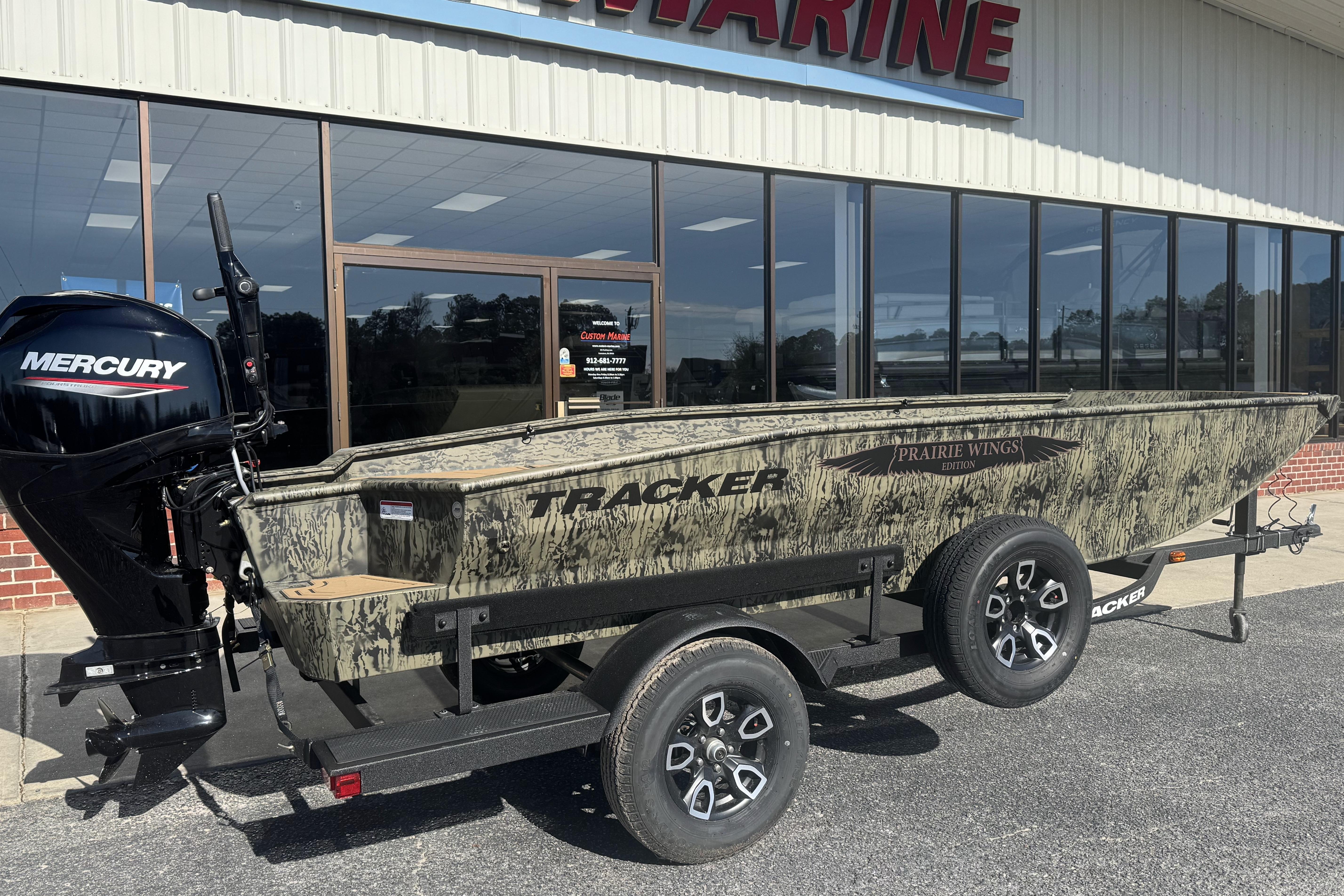 2026 Tracker Grizzly 1650 T Prairie Wings Edition boat with Mercury engine, parked outside a marine store.