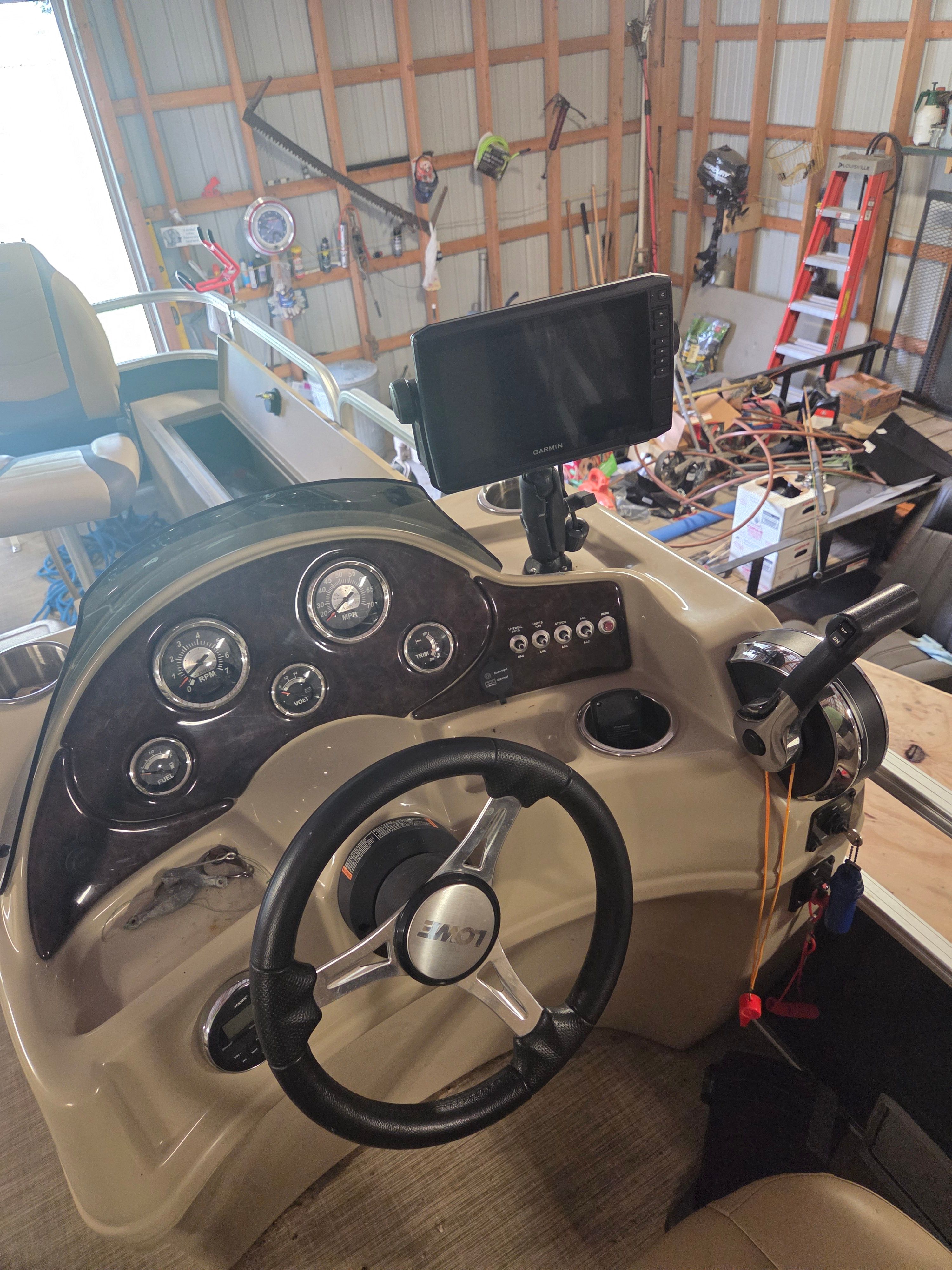The cockpit of a boat with a steering wheel, gauges, and a screen.