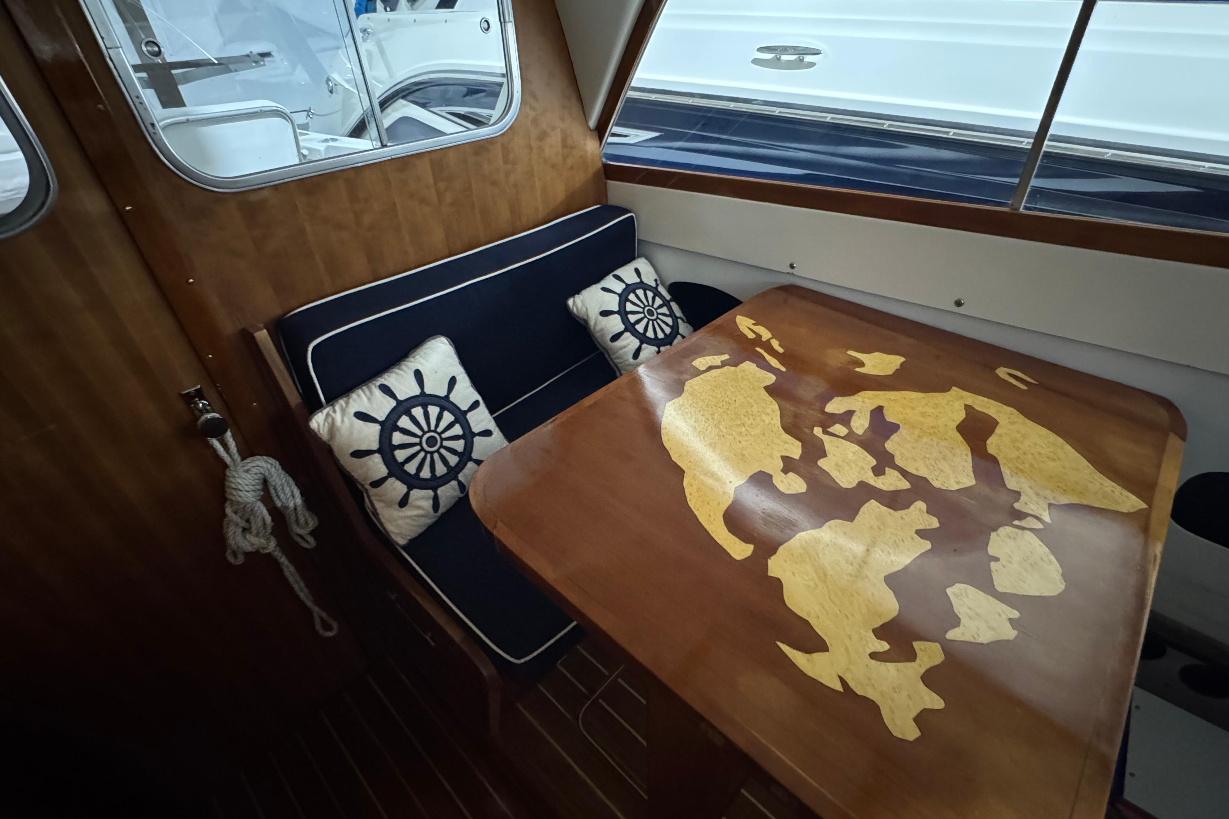 1974 Bertram 31 Flybridge Cruiser interior with nautical-themed cushions and a wooden table.