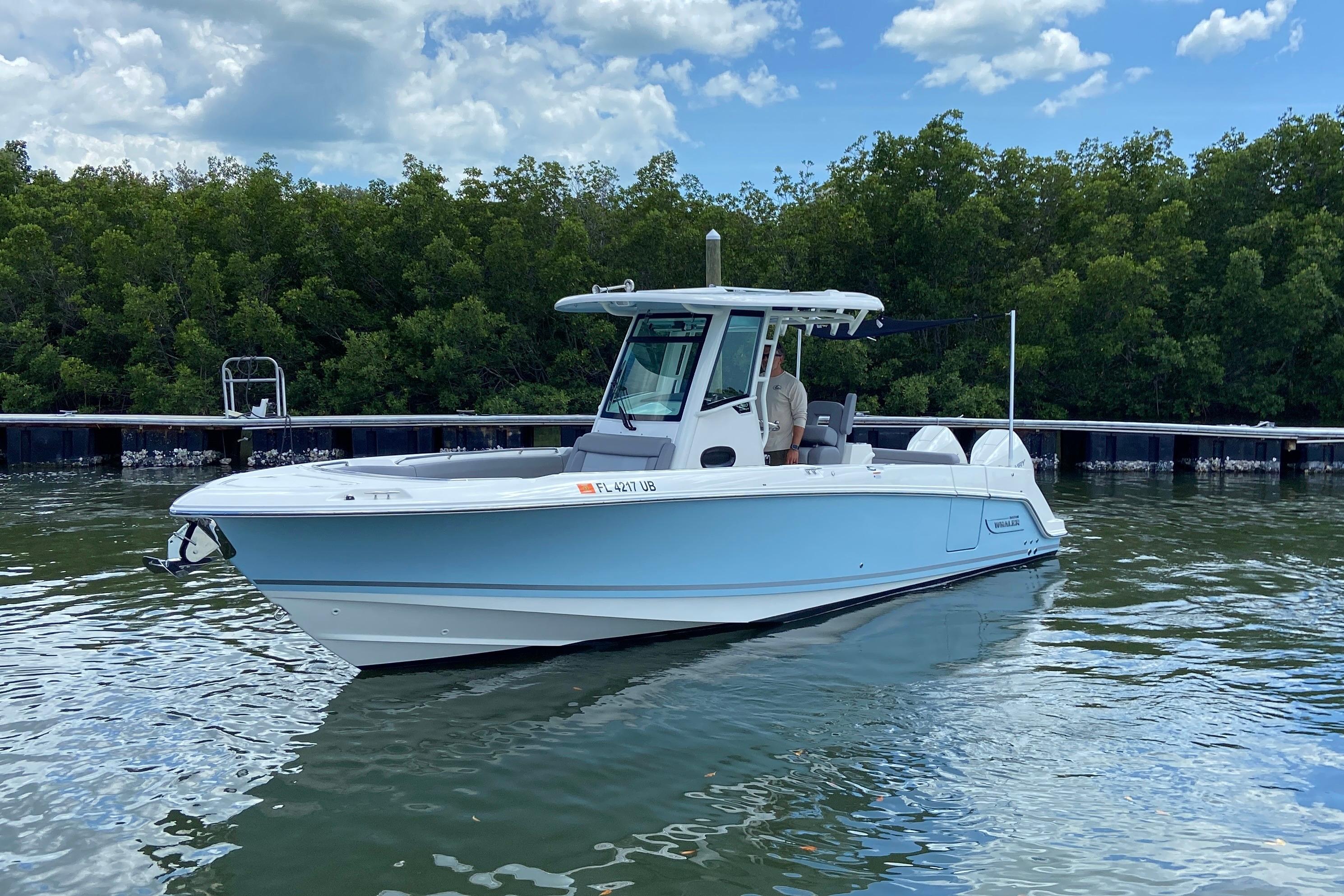 2025 Boston Whaler 280 Outrage boat on calm water near a dock.