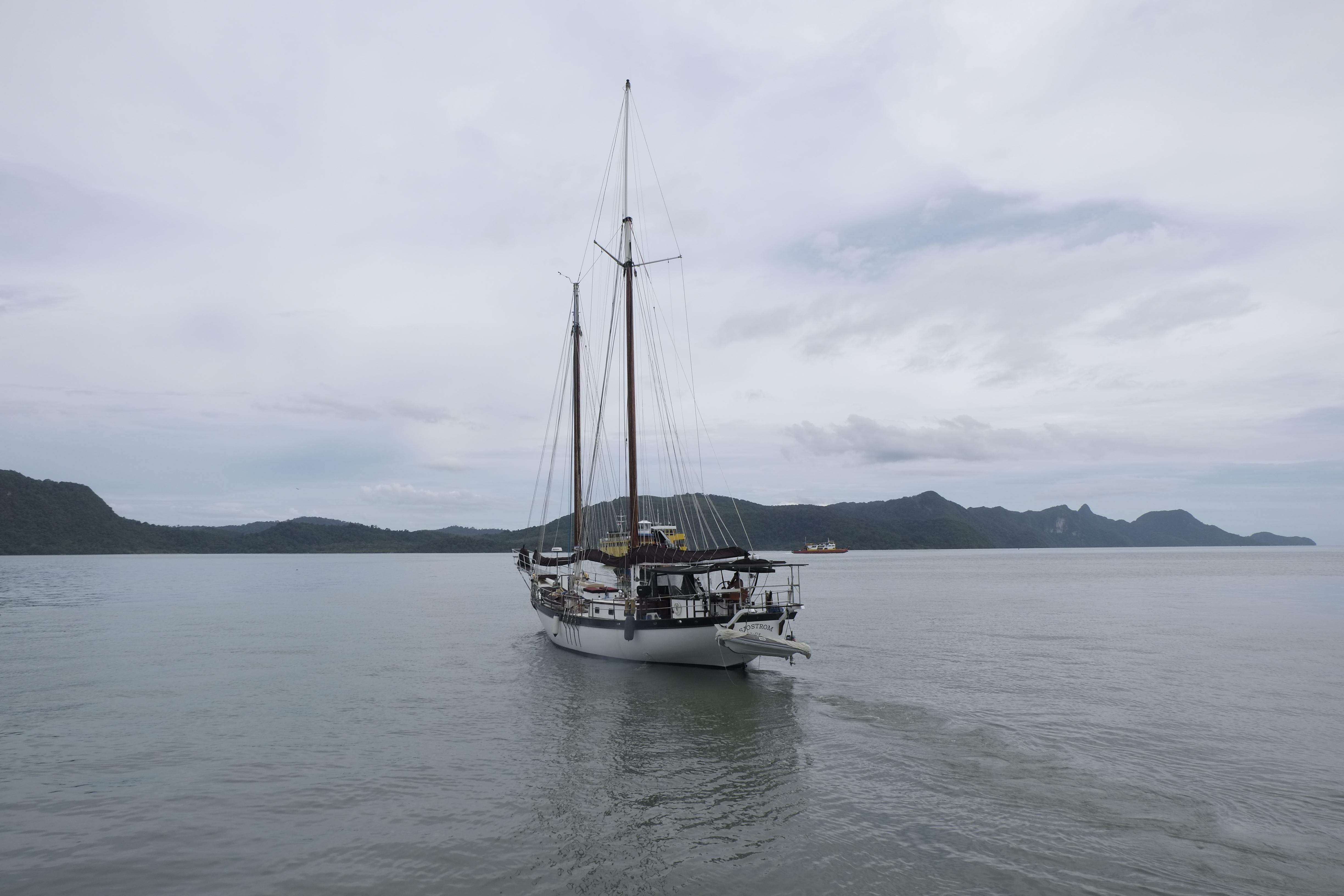 Custom Bud Macintosh schooner sailing on calm waters, overcast sky, distant hills in background.