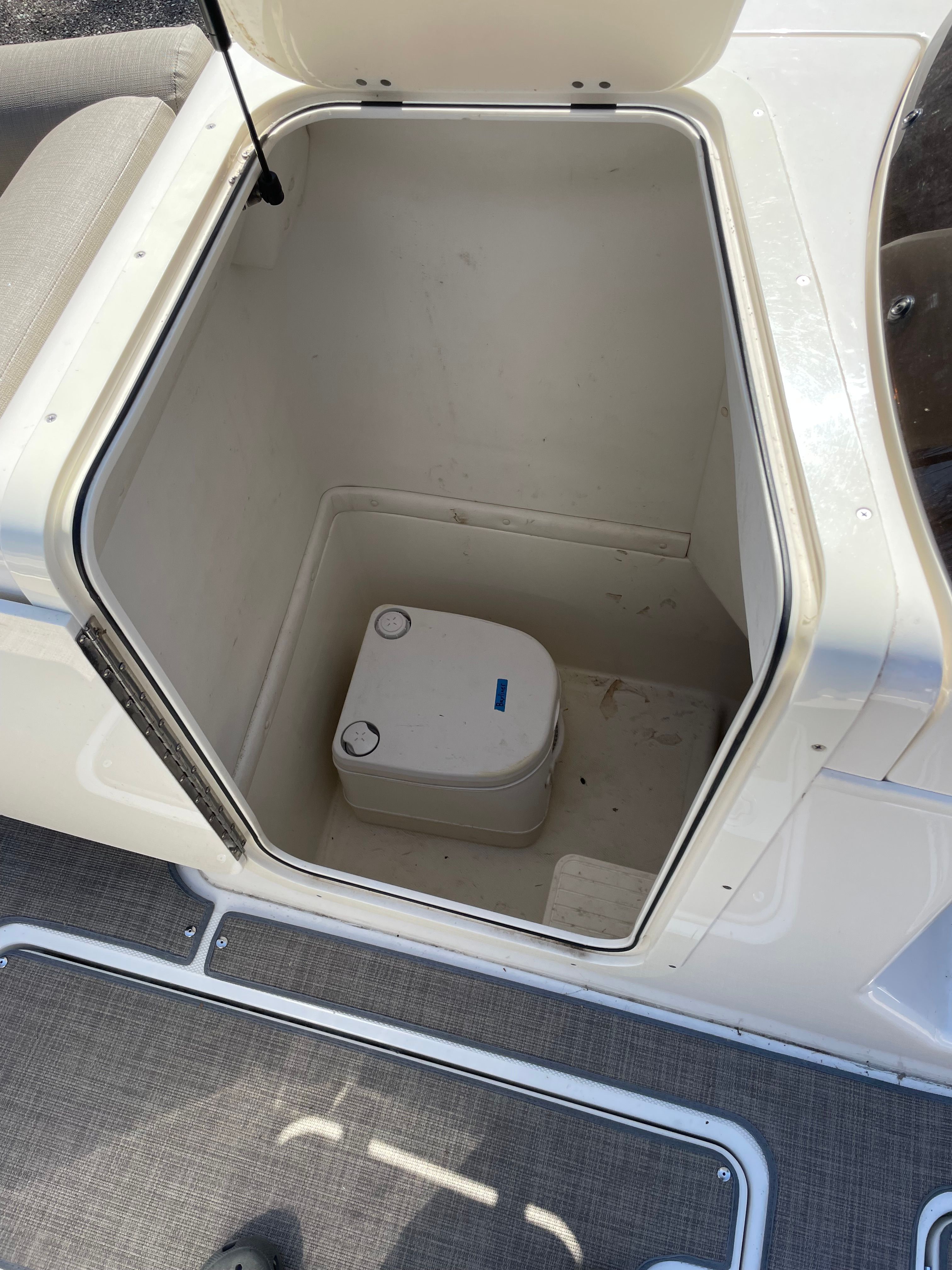 An open storage compartment on a 2016 Bayliner Element XR7 boat with a portable toilet.