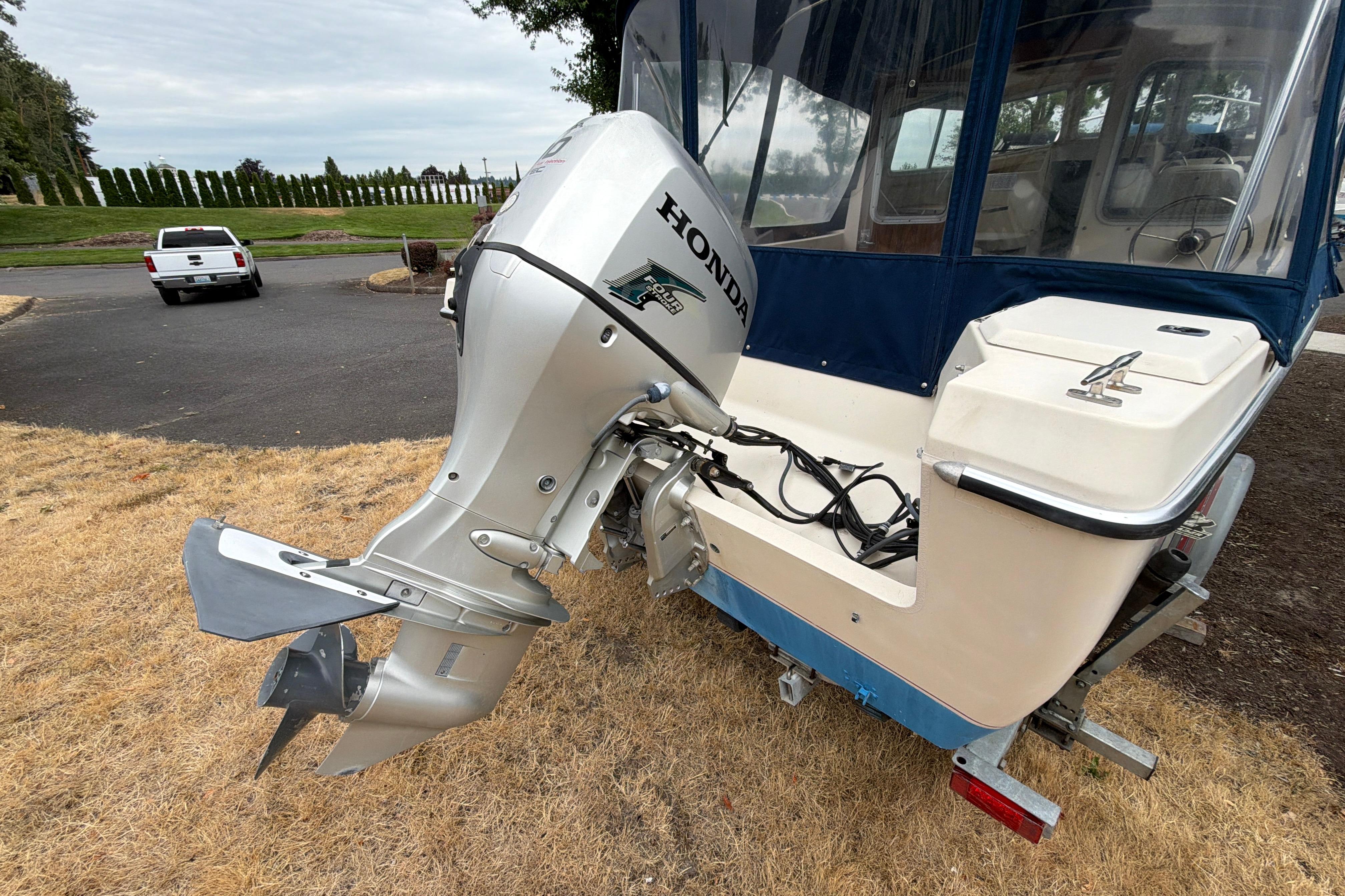 1989 C-Dory 22' Angler with Honda outboard motor on trailer, parked on grass.