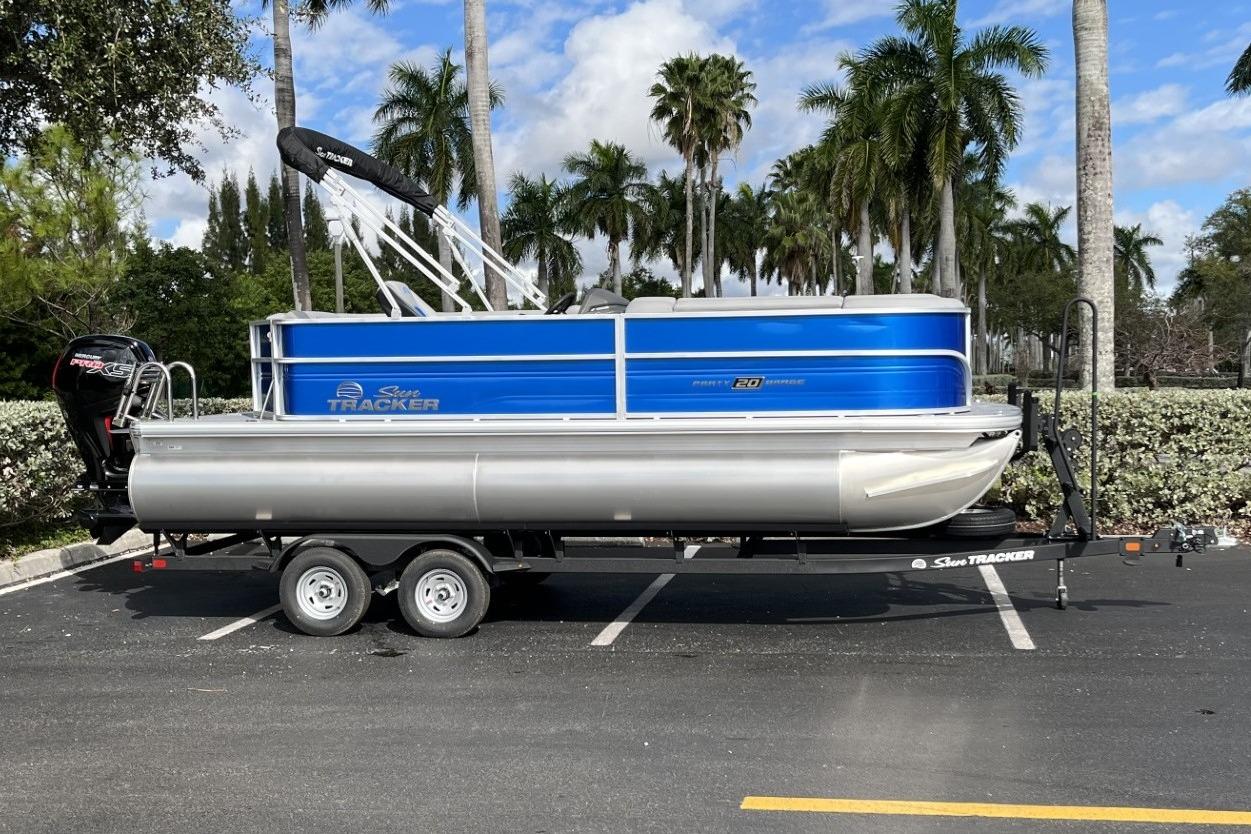 2026 Sun Tracker Party Barge 20 DLX pontoon boat on trailer, parked with palm trees.