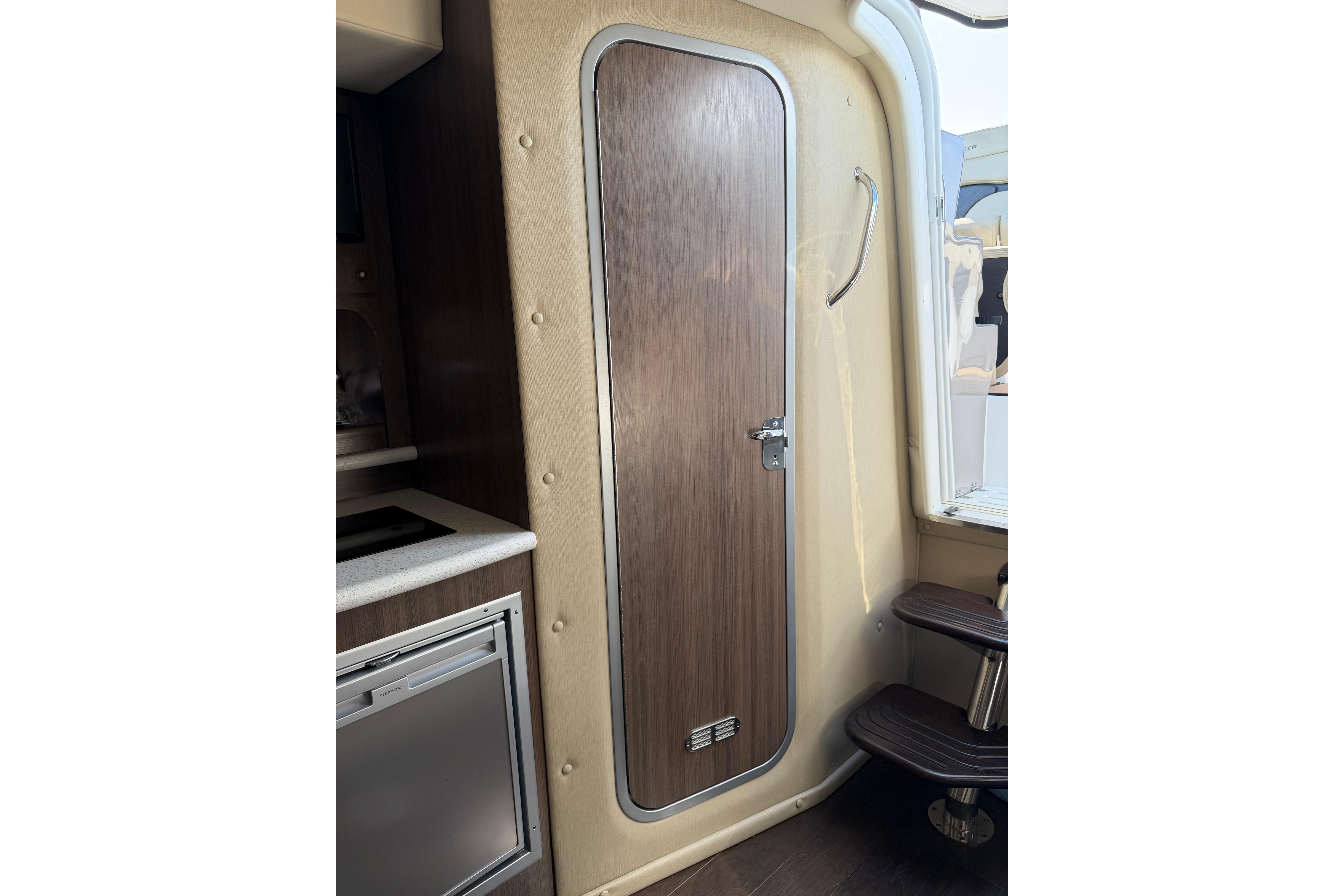 2019 Rinker EX 320 cabin interior with wooden door and compact kitchenette.