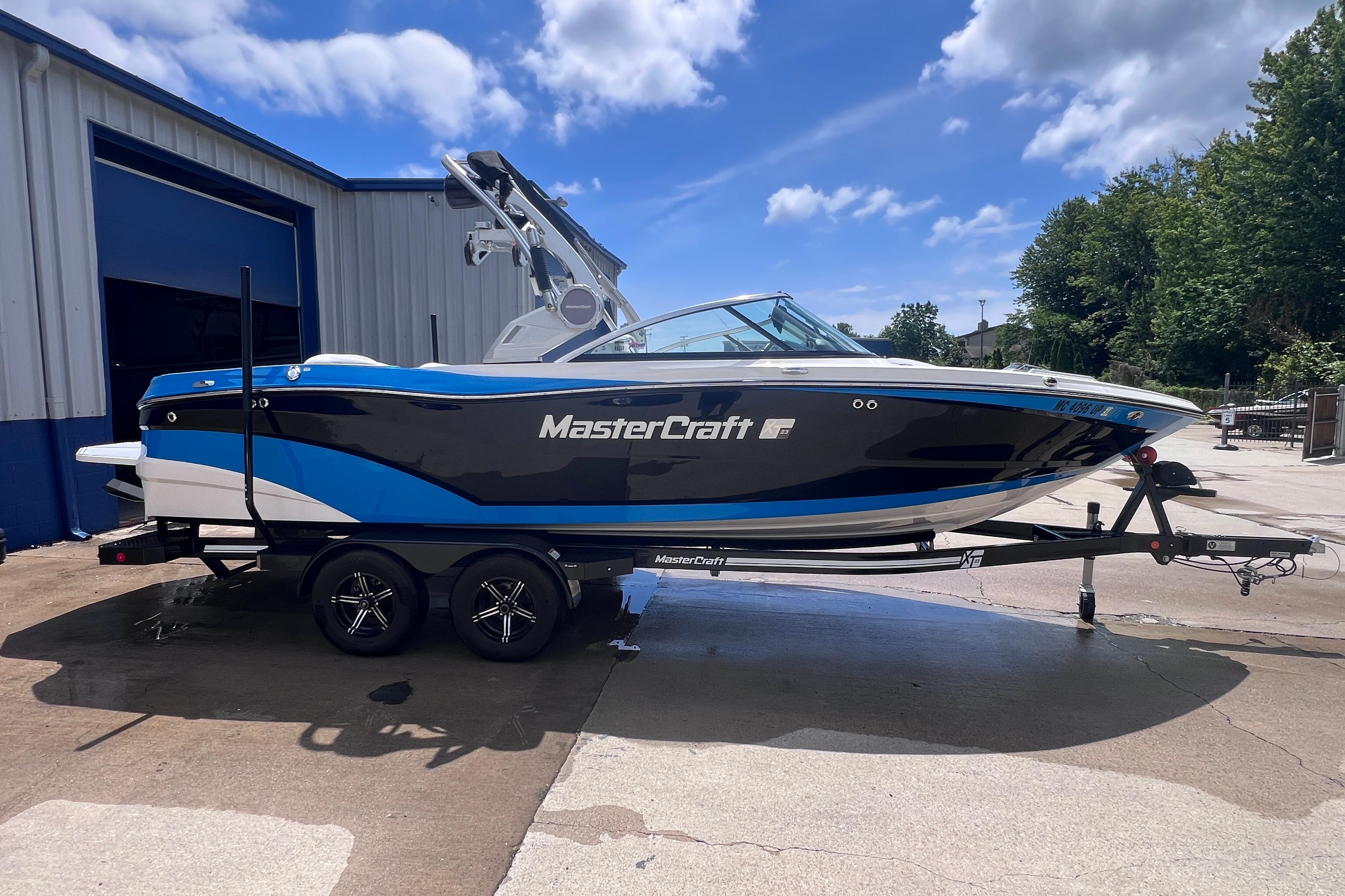 2021 MasterCraft XT23 boat on trailer, parked outside a building under a blue sky.
