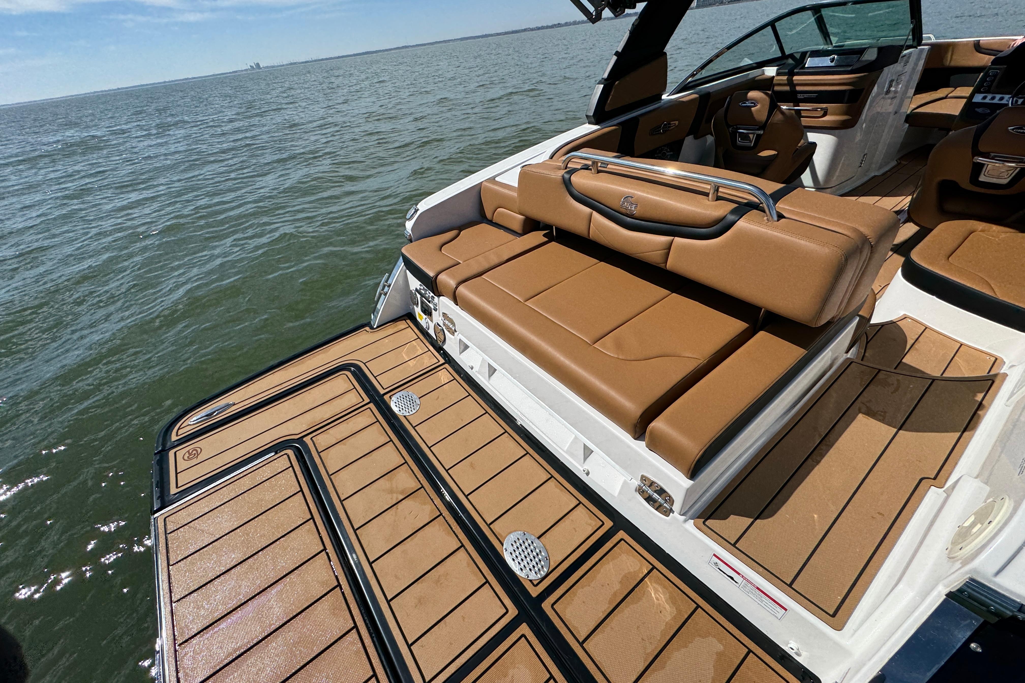 2023 Chaparral 26 Surf boat with tan seating and deck, overlooking calm waters.