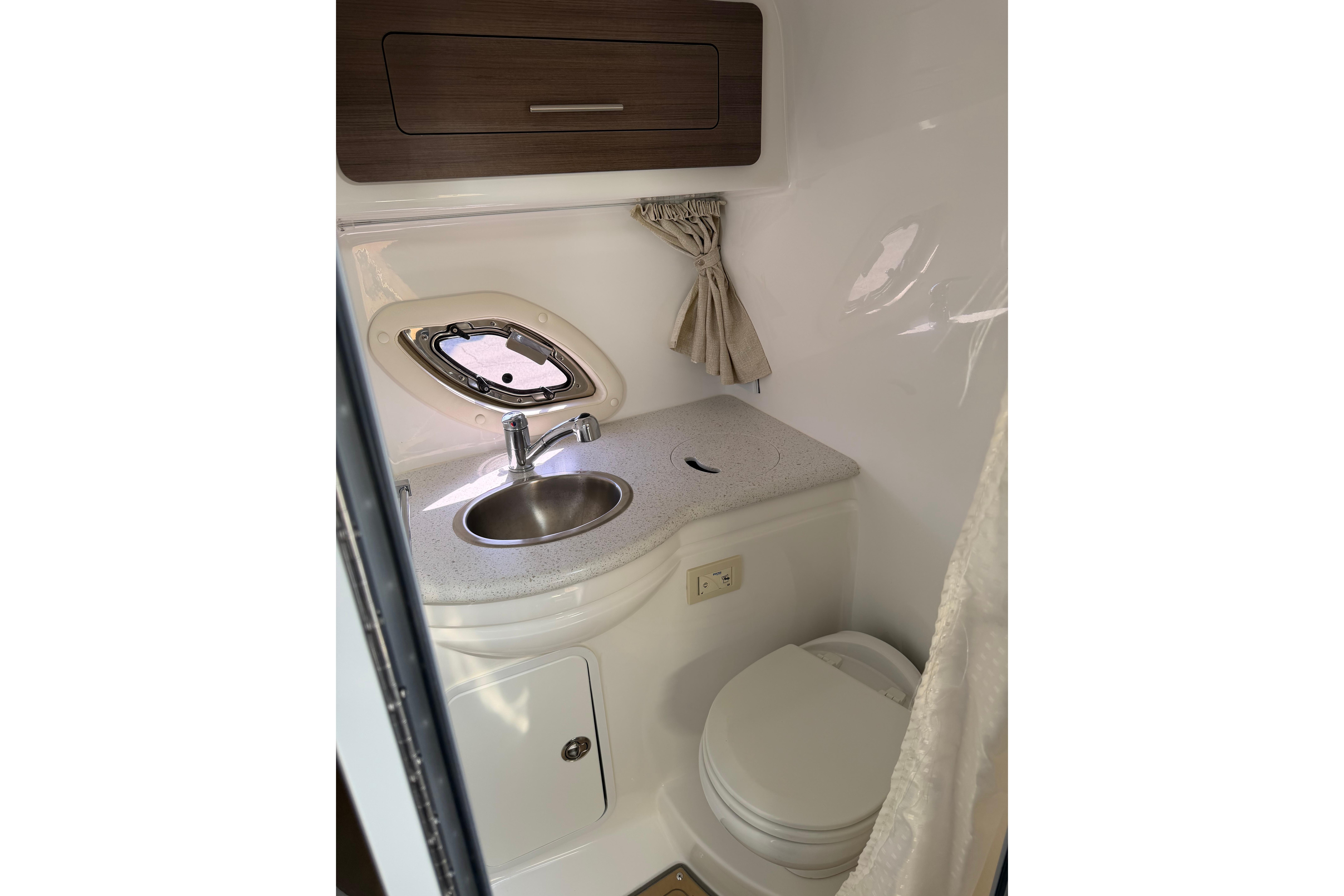 2019 Rinker EX 320 boat bathroom with sink, toilet, and porthole window.