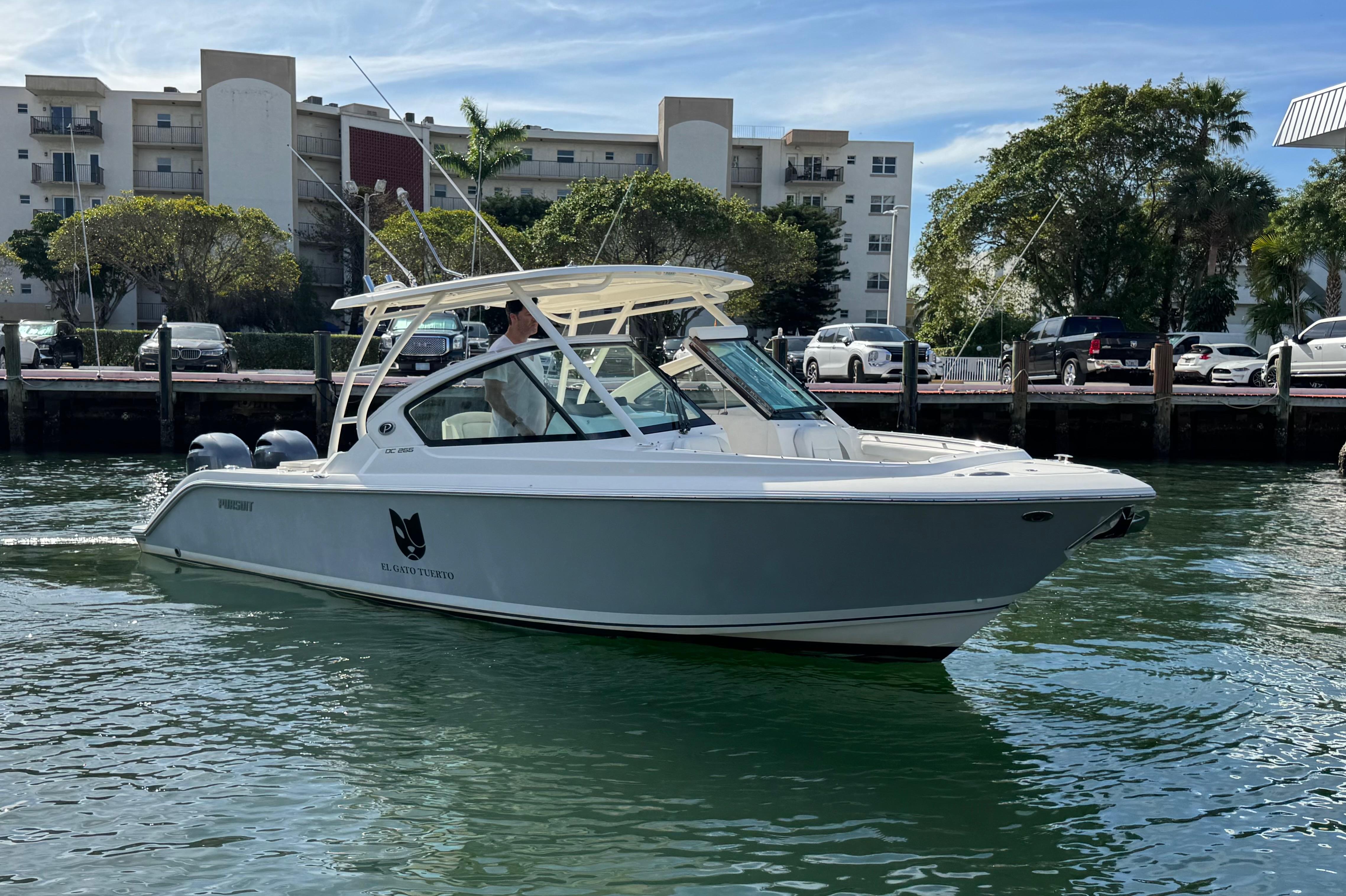 2022 Pursuit DC 266 Dual Console boat on water near dockside buildings.