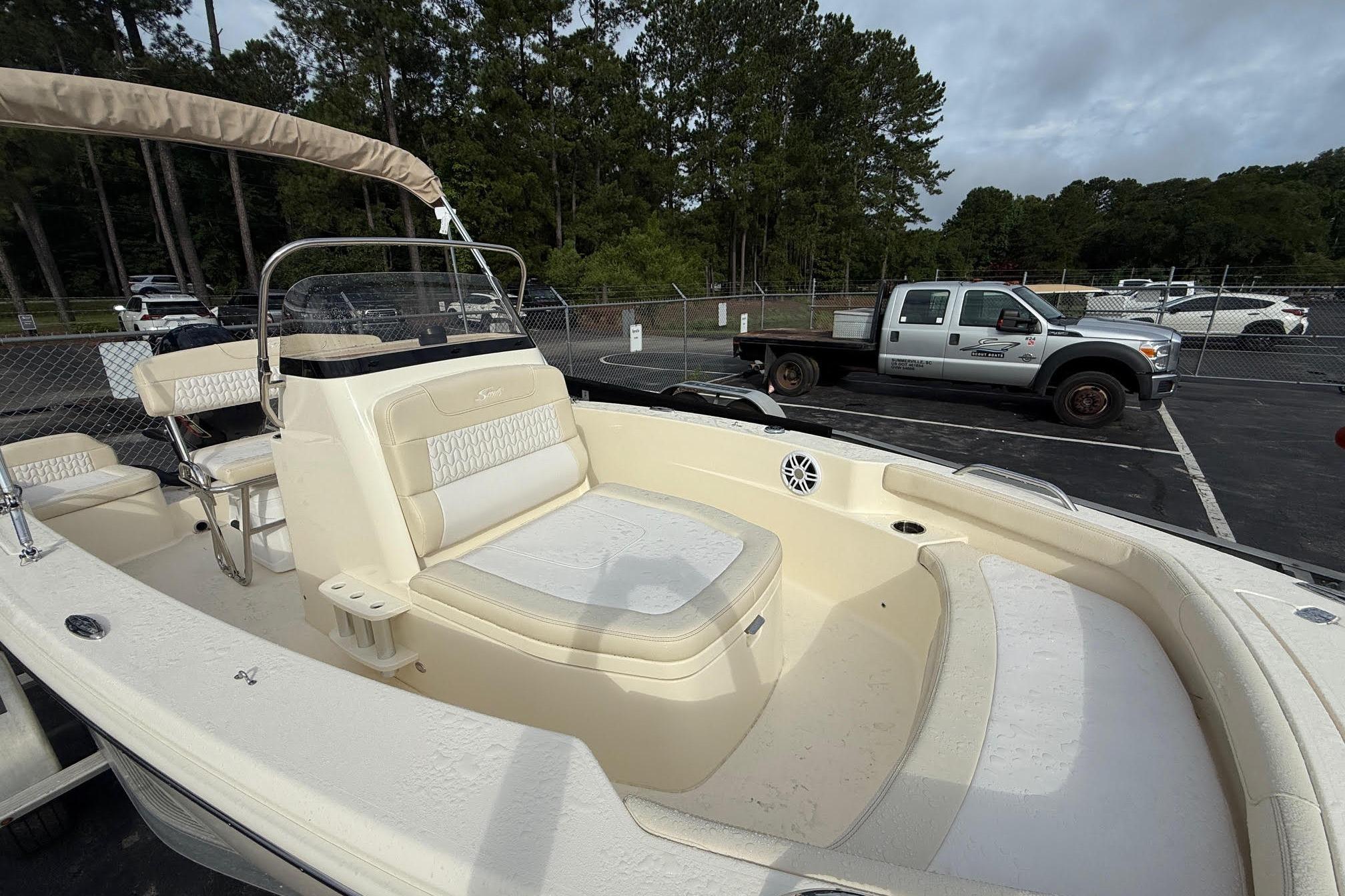 2026 Scout 188 Sportfish boat with seating, parked in a lot with trees and vehicles.