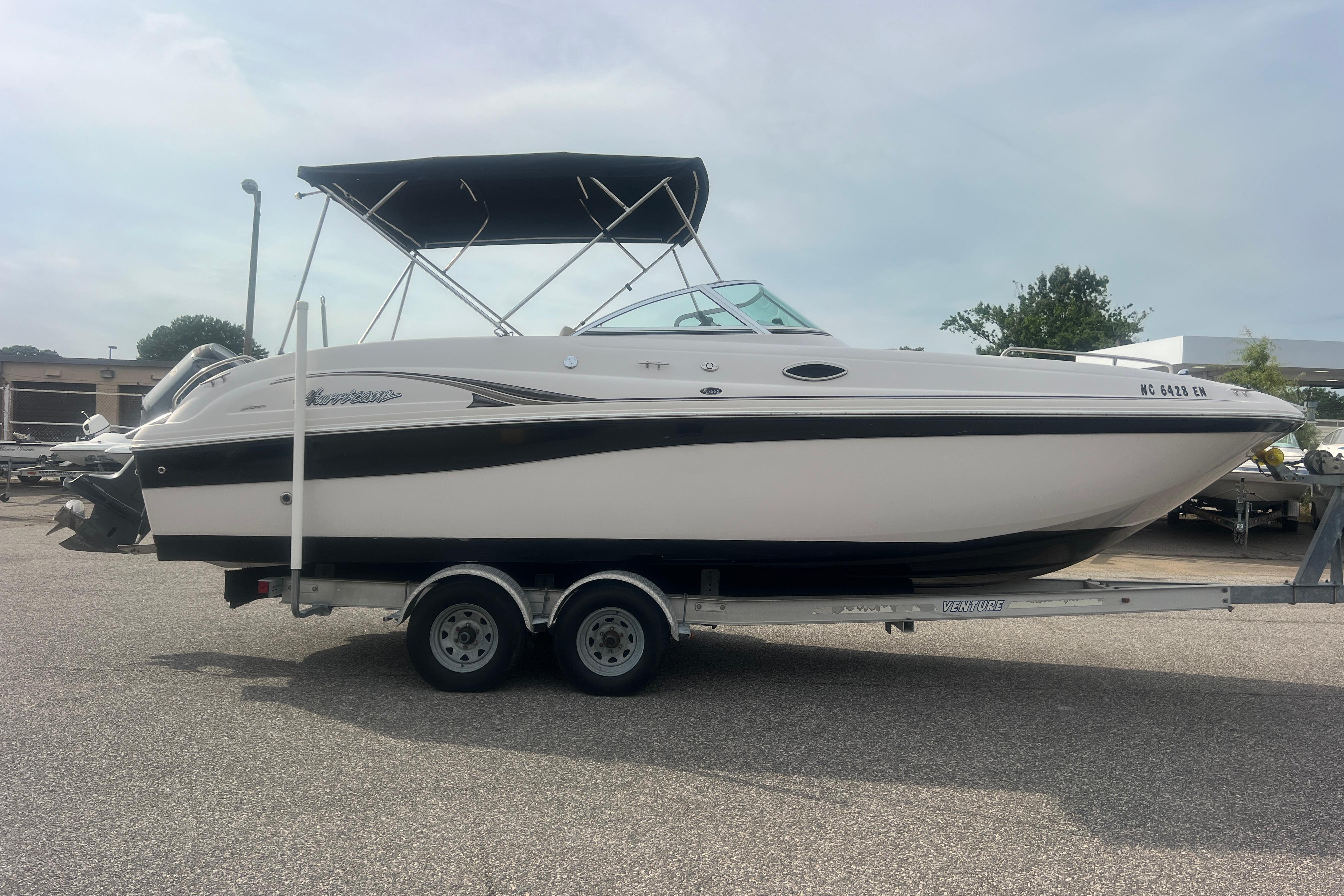 2002 Hurricane SunDeck 260 OB boat on trailer, parked outdoors under cloudy sky.