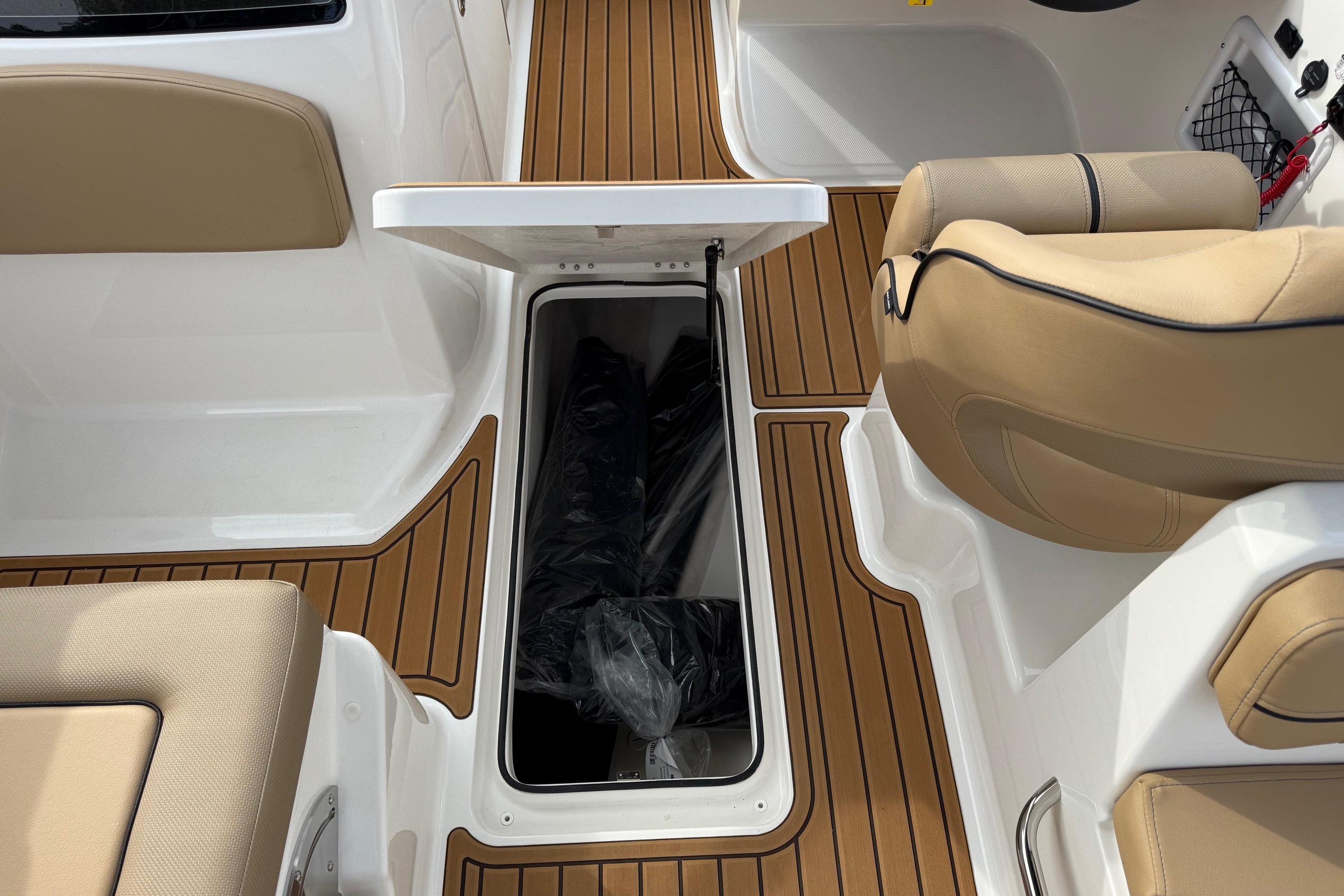 2026 Bayliner VR6 Bowrider OB interior with open storage compartment and tan seating.