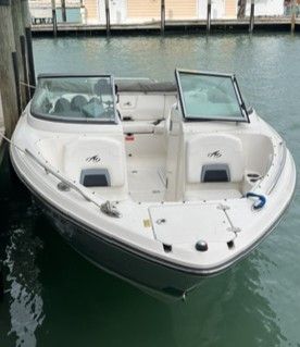 A white sport boat is docked in the water. It features an open cabin and dual windshields.
