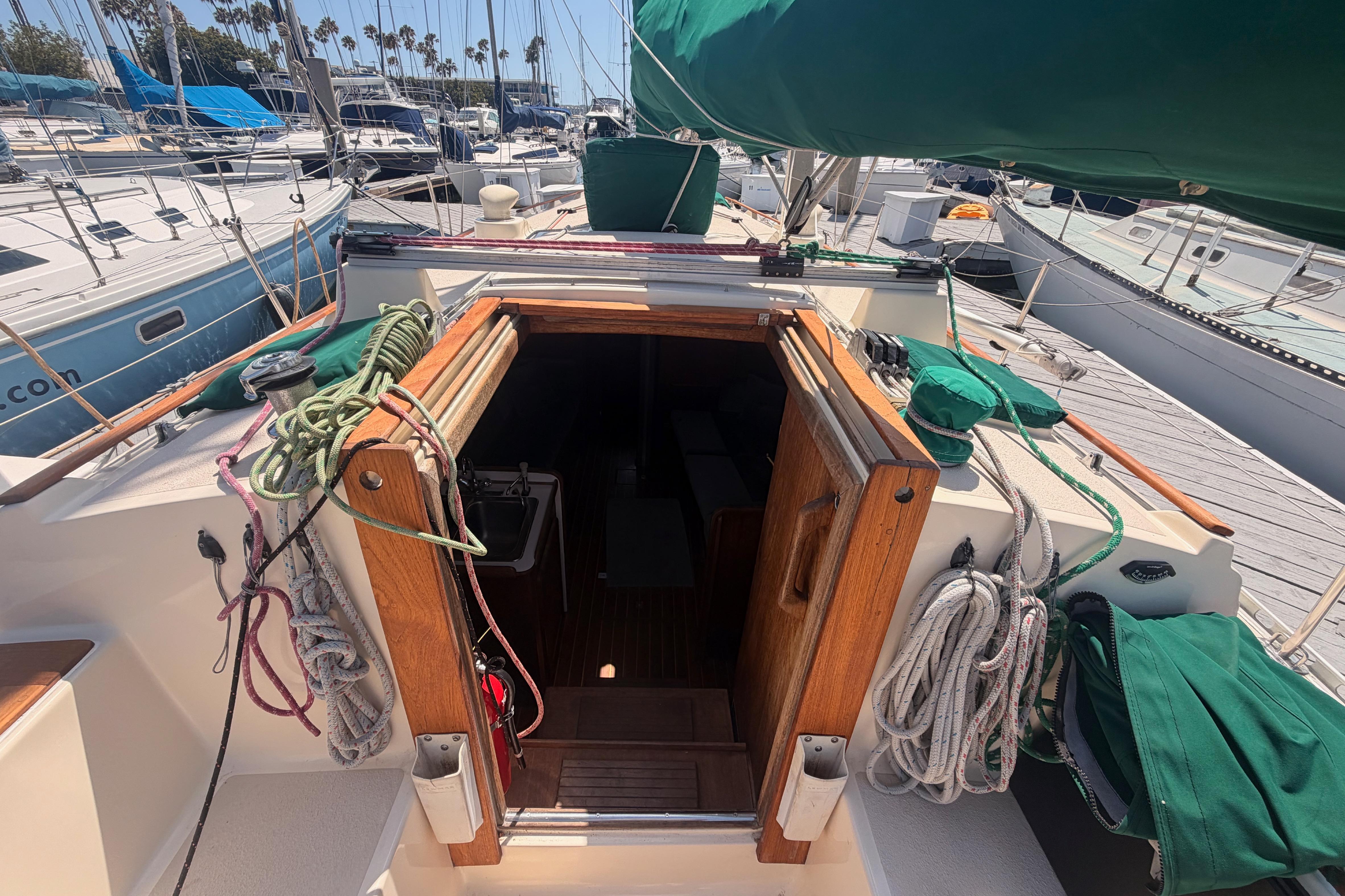 Sailboat deck view of 1991 Caliber 33, featuring ropes and open cabin entrance.