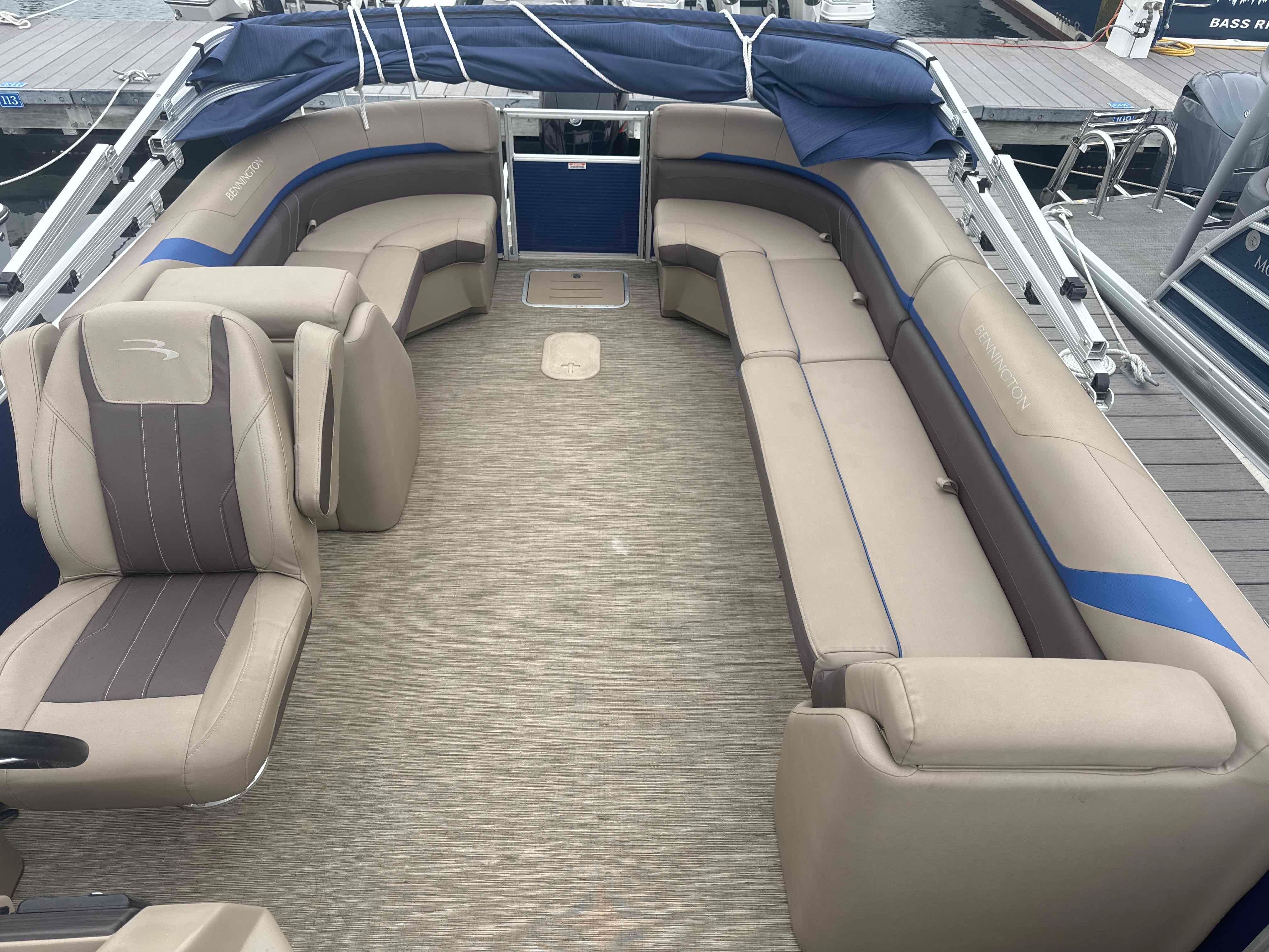 The image shows the spacious deck of a Bennington 23SXSRC pontoon boat with beige upholstery.