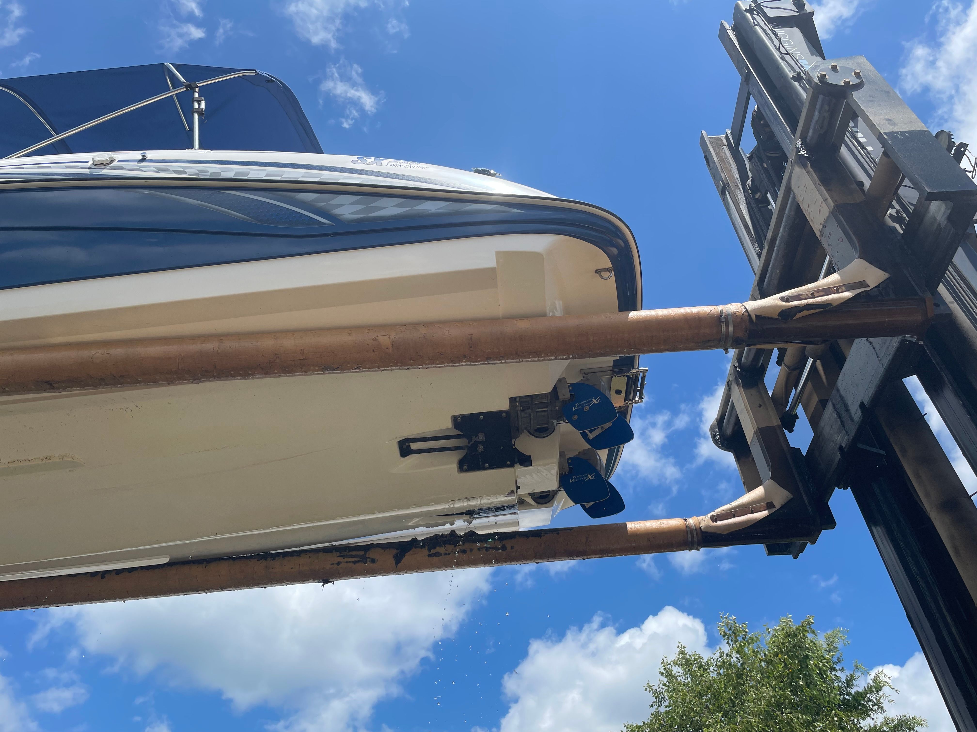 A 2006 Yamaha SX230 boat being lifted by a forklift, set against a blue sky.