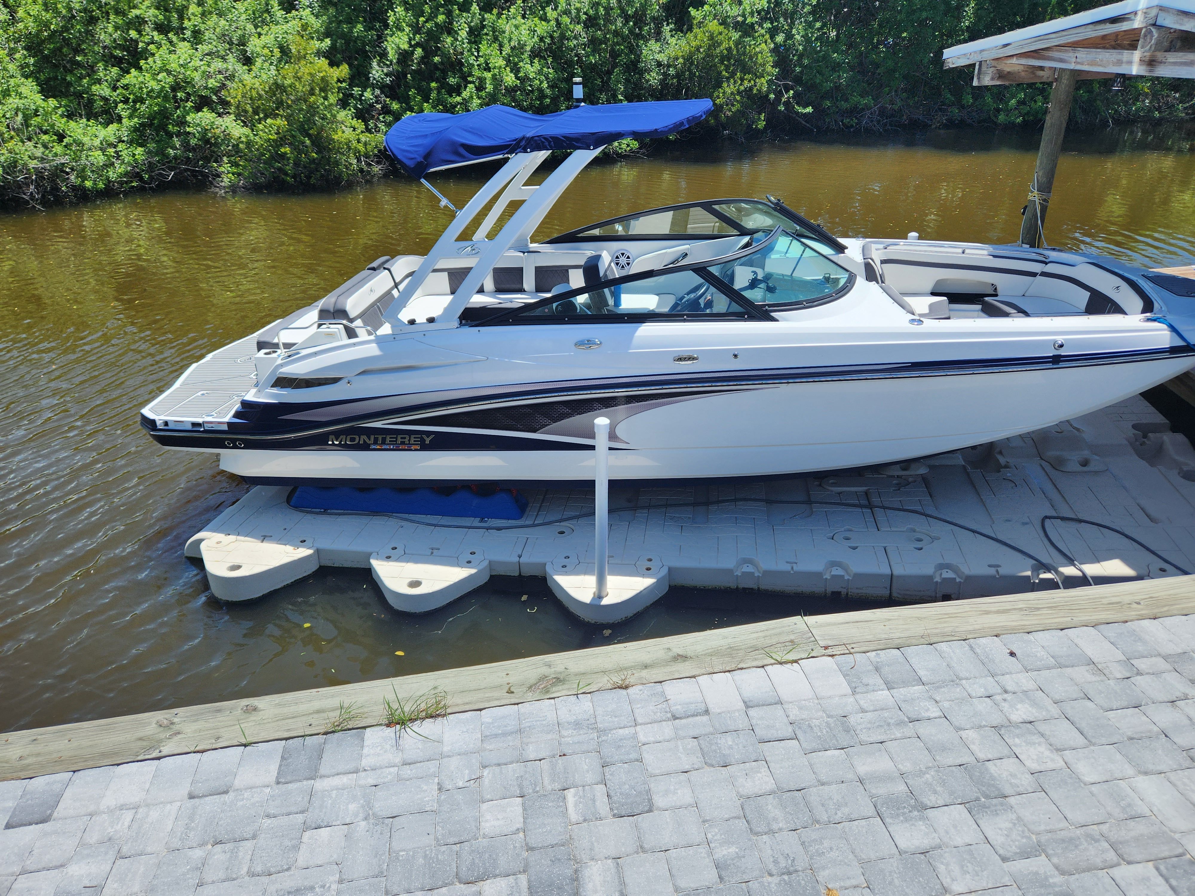 A 2021 Monterey M6 boat docked. It features a blue canopy and sleek lines.