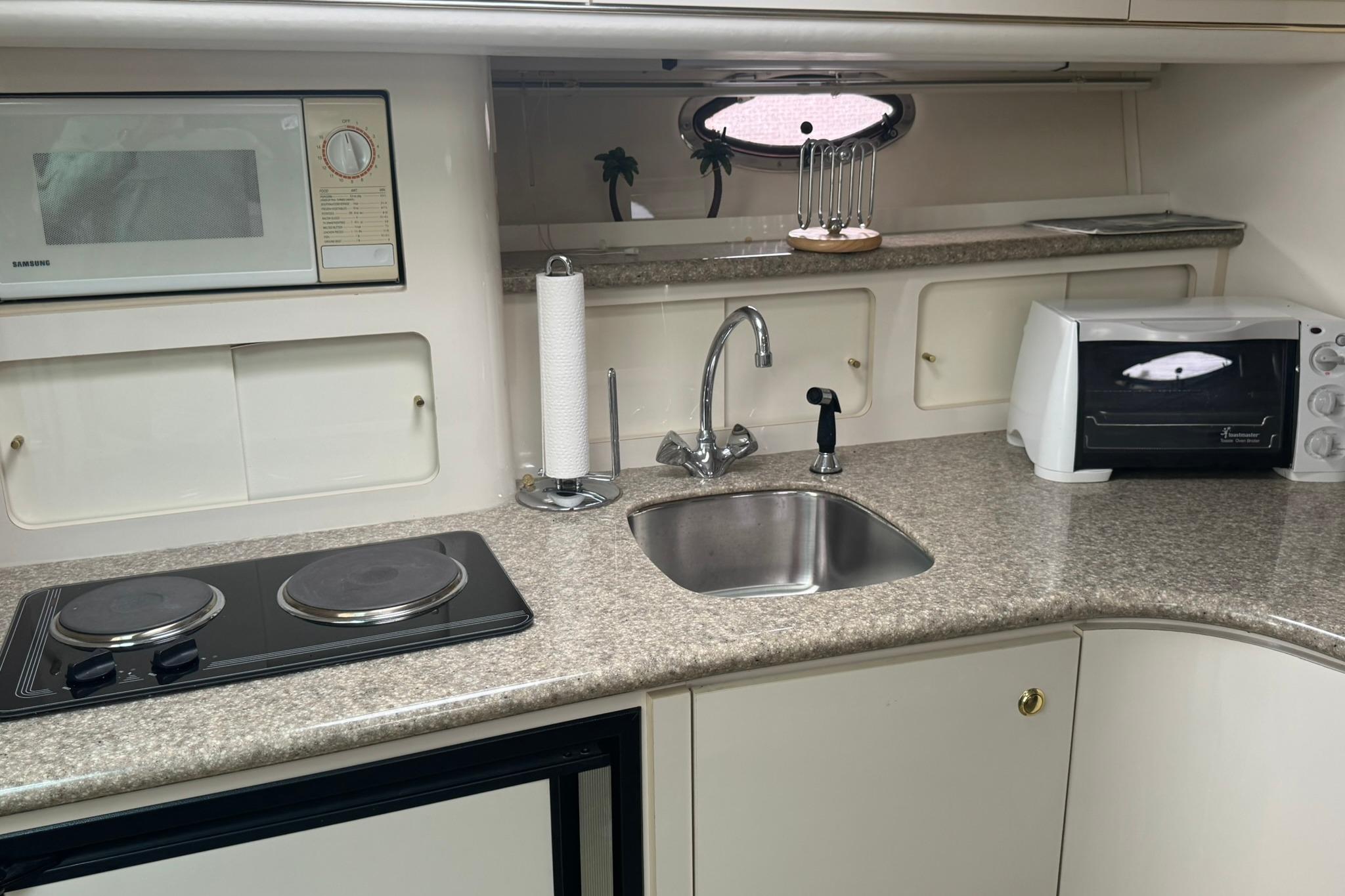 1998 Maxum 3700 SCR yacht kitchen with stove, sink, microwave, and toaster oven.