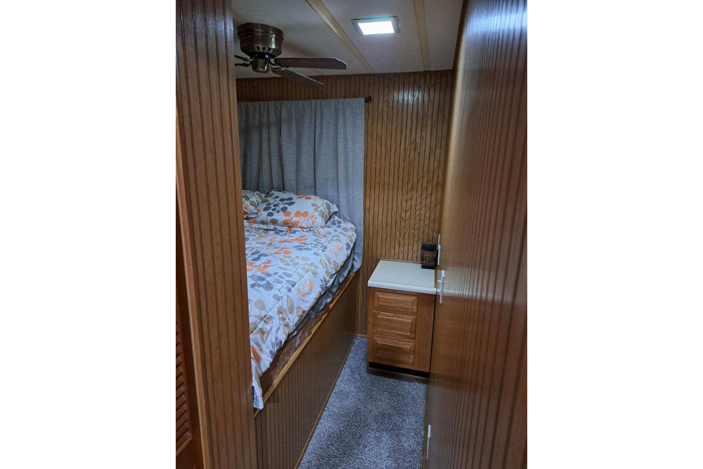 Cozy bedroom interior of 1990 Sumerset 16 x 70 houseboat with wood paneling and floral bedding.