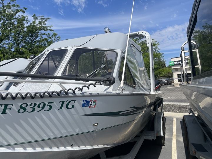 A silver motorboat with an enclosed cabin is on a trailer in a parking lot.