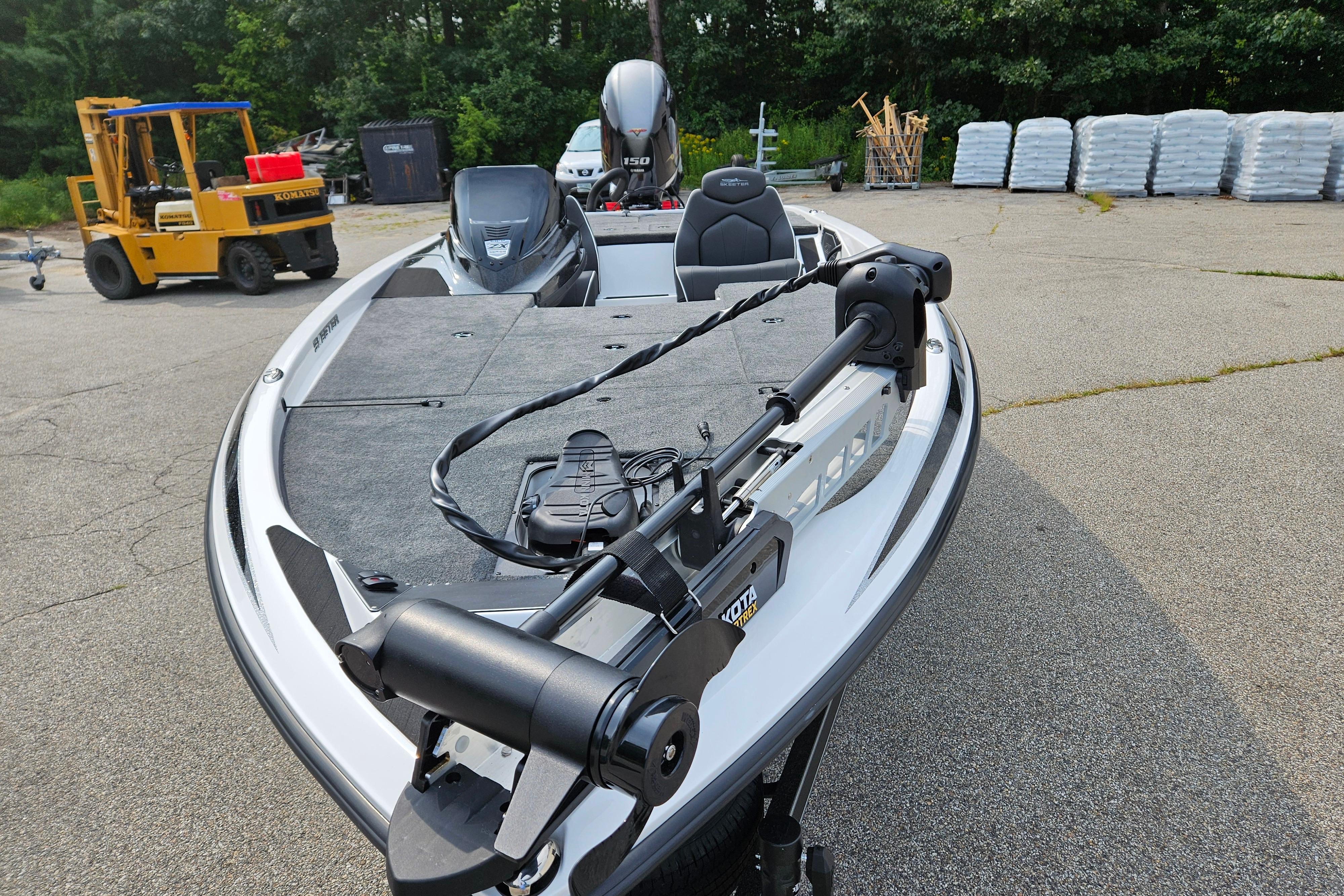 2026 Skeeter ZX150 boat with trolling motor, parked on pavement near forklift and stacked materials.