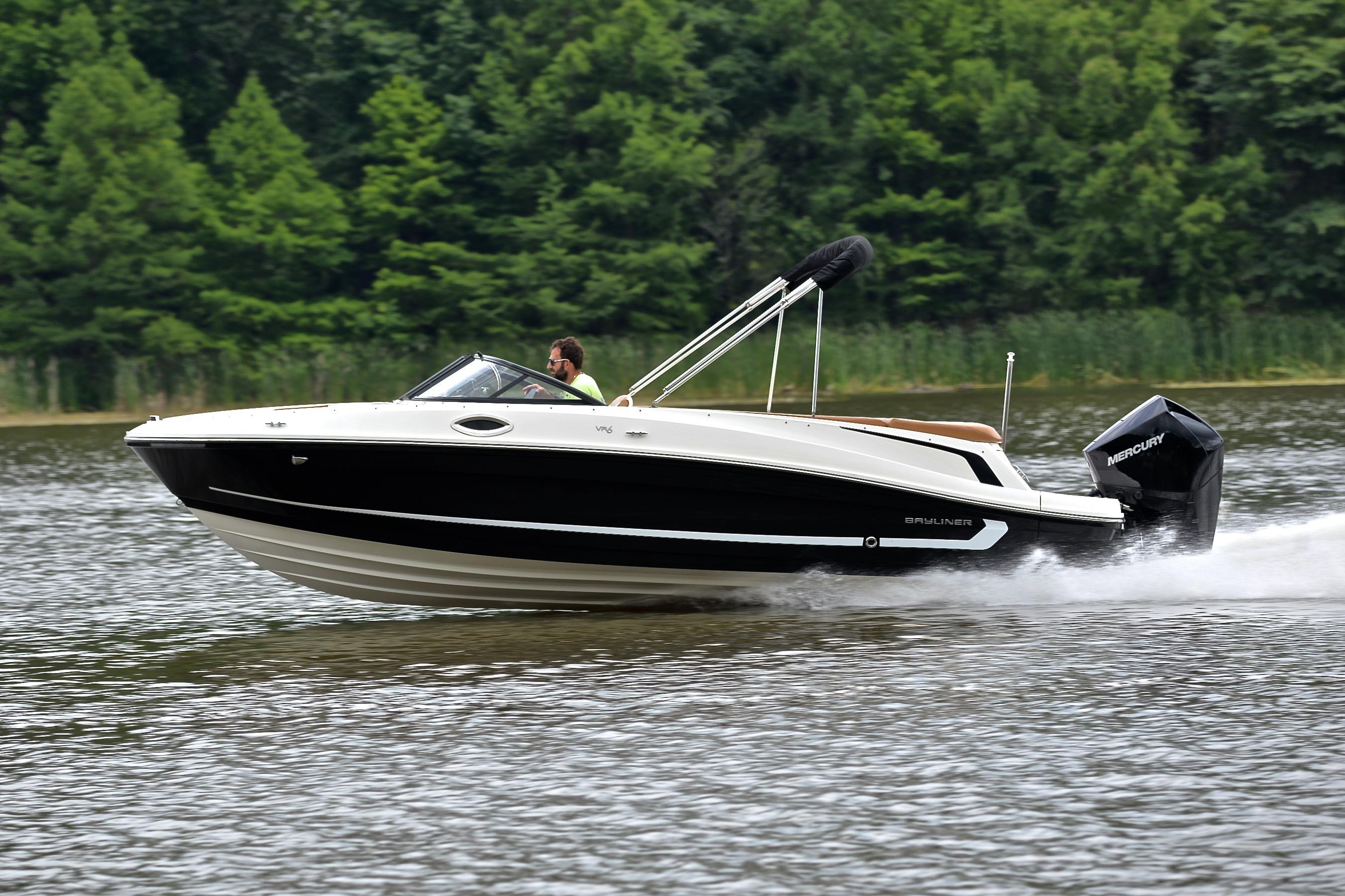 2019 Bayliner VR6 Bowrider OB cruising on a lake with lush green forest backdrop.