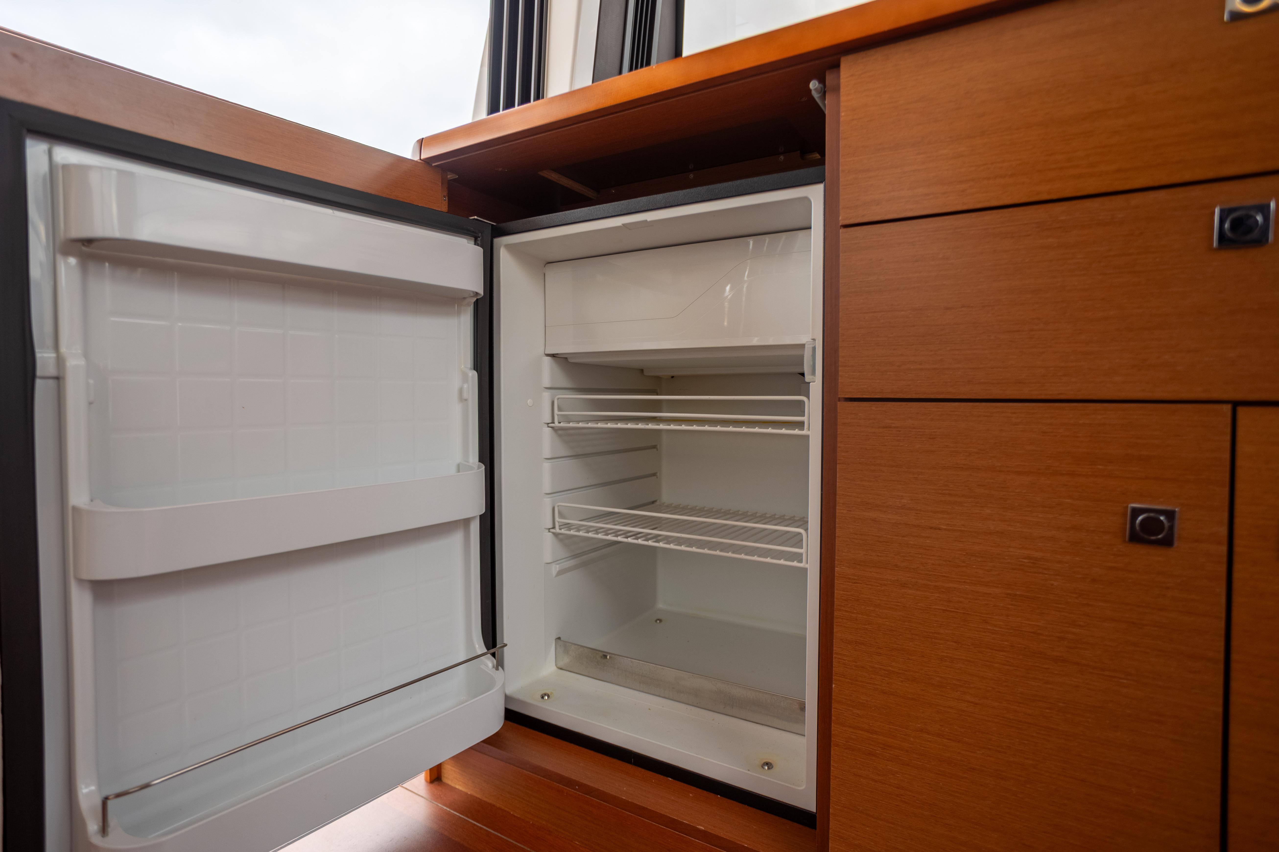Open refrigerator in 2017 Jeanneau NC 14 yacht interior, showcasing wooden cabinetry.