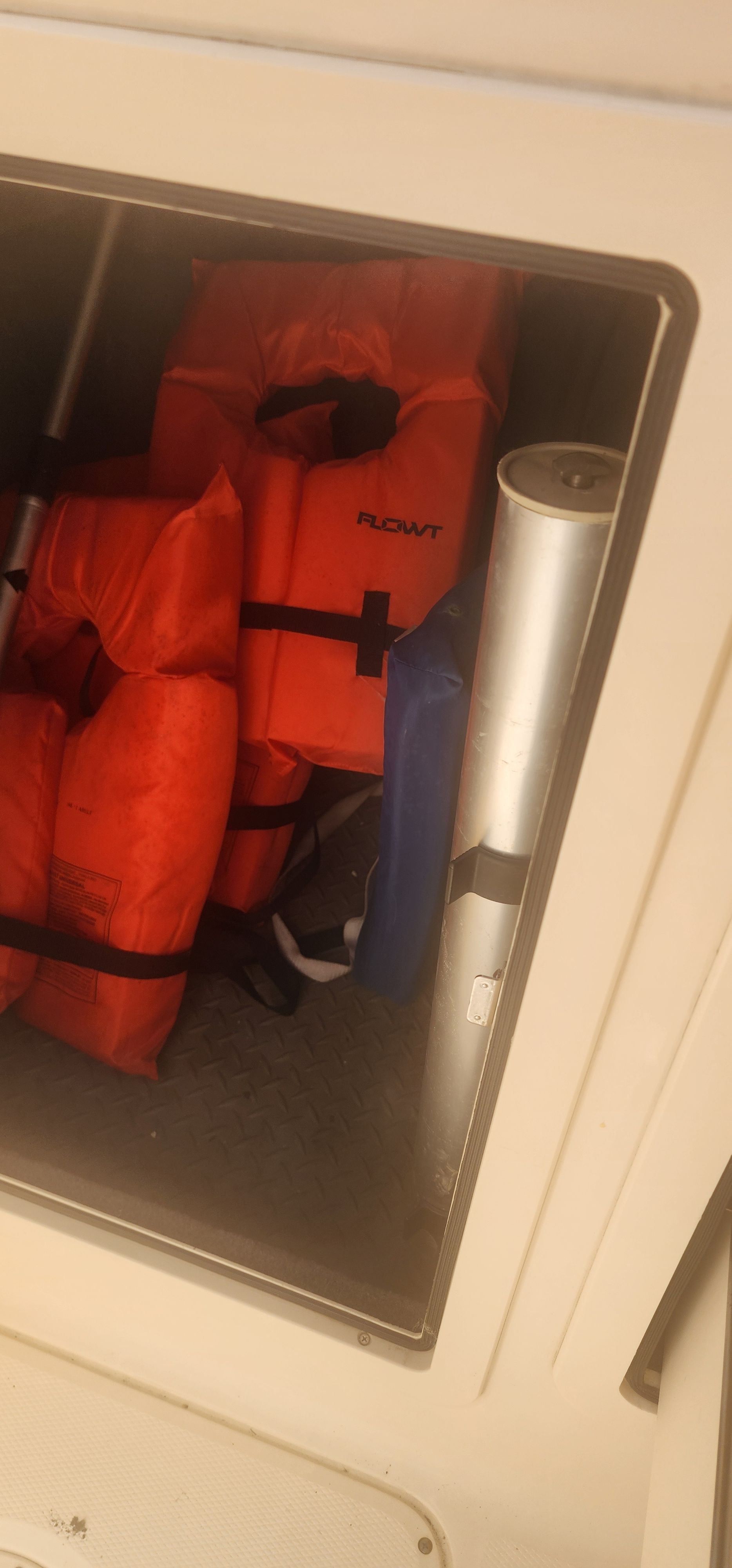 A storage compartment with several orange life jackets and a blue item.