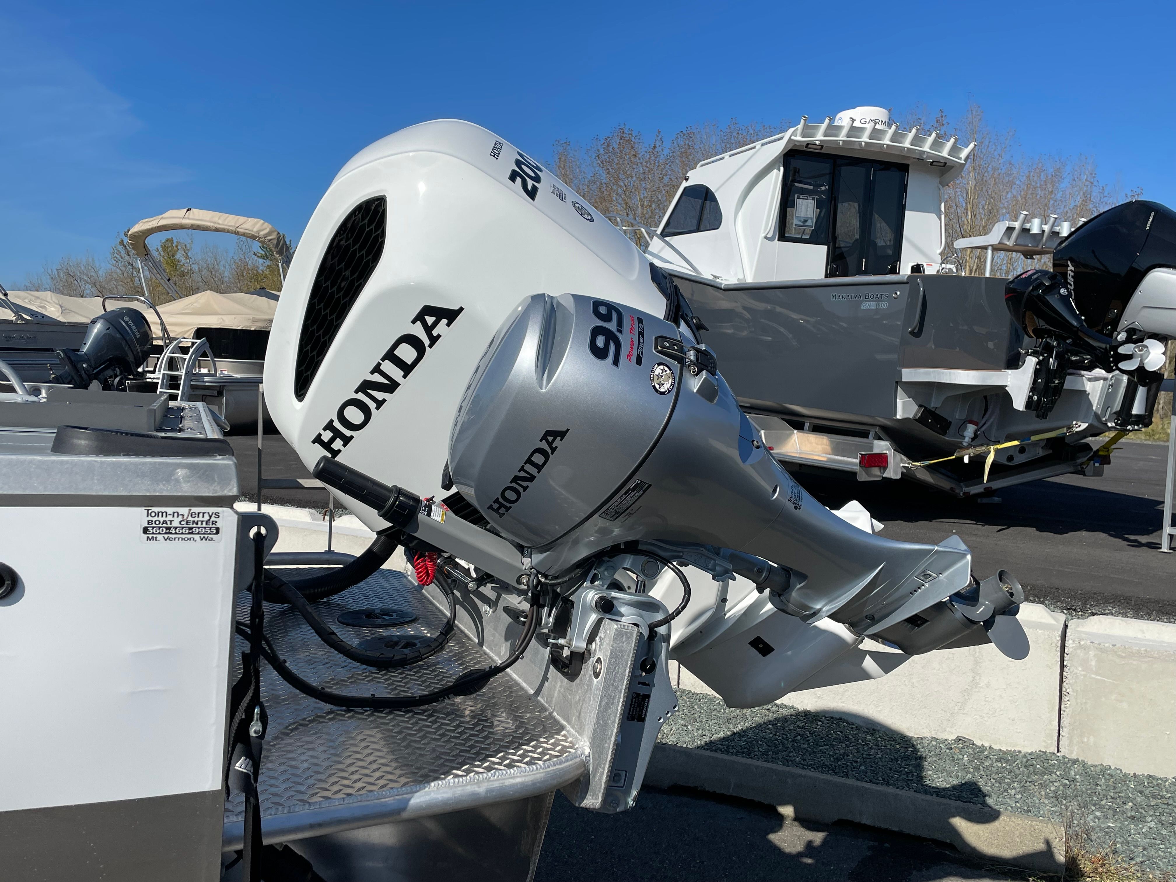 A Honda outboard motor is attached to a boat parked on a lot, with other boats in the background.