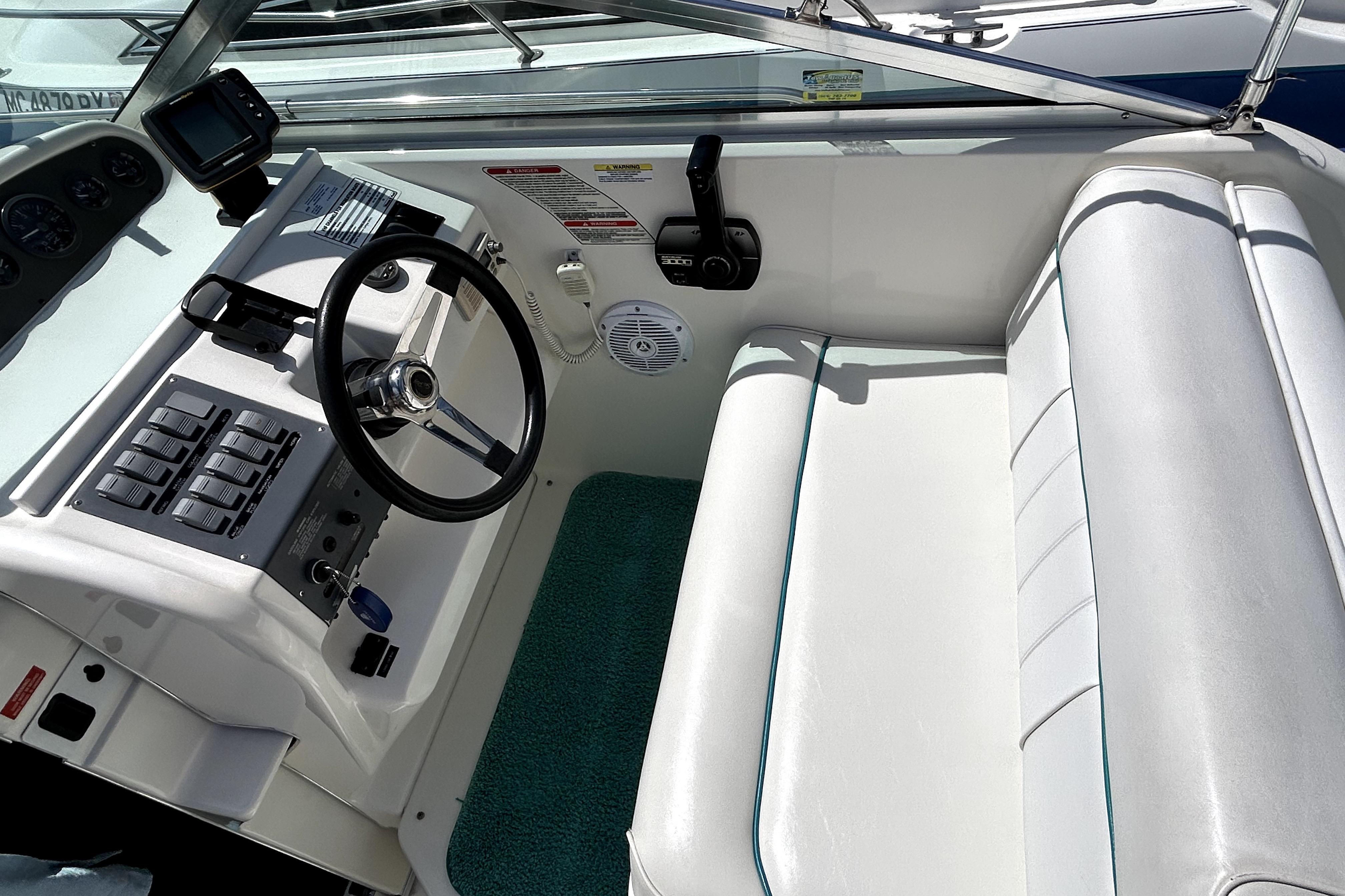 1995 Sea Ray 250 Sundancer helm with steering wheel, controls, and white seating.