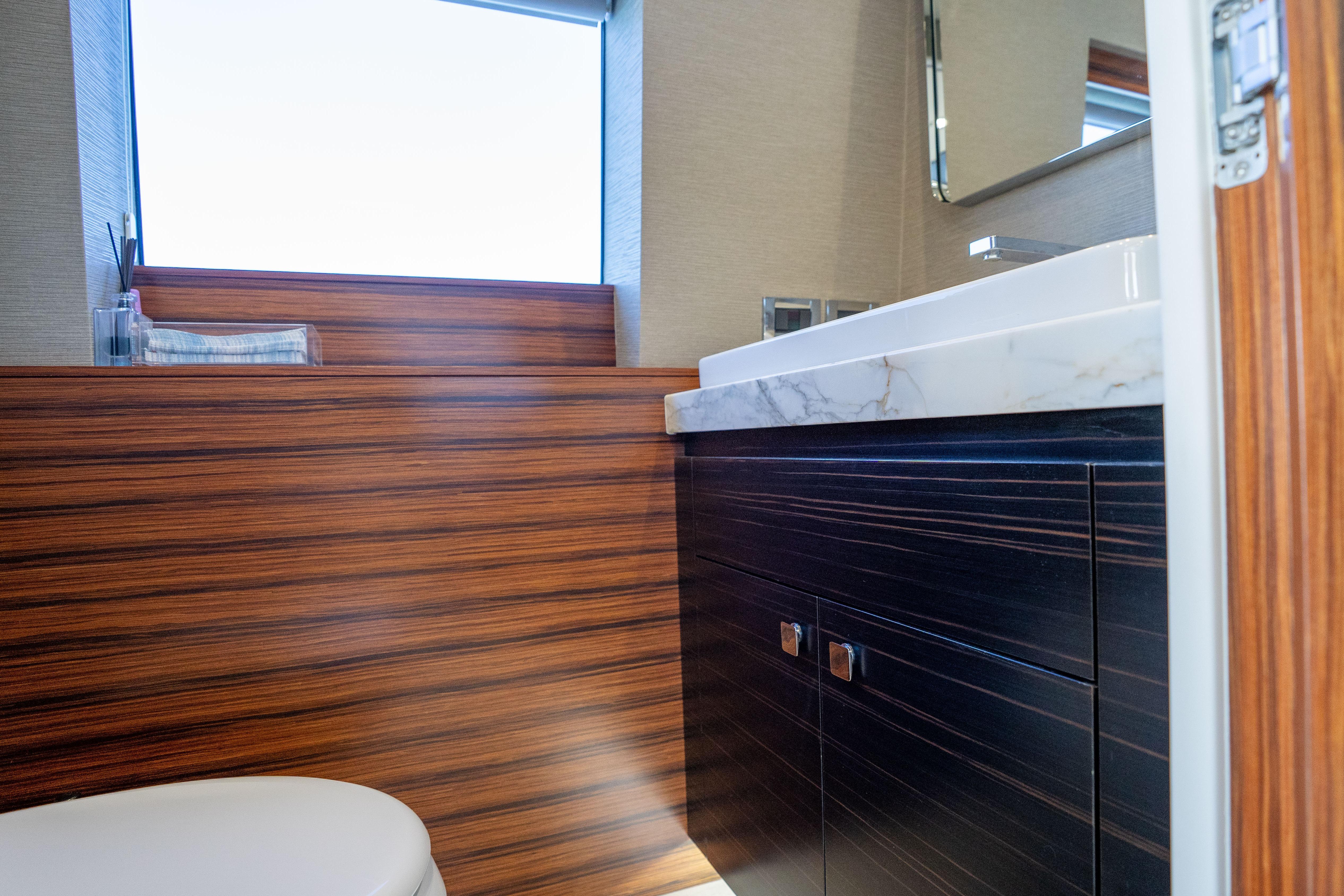 Luxurious bathroom interior of 2021 Hatteras M75 Panacera yacht with wood accents and marble countertop.