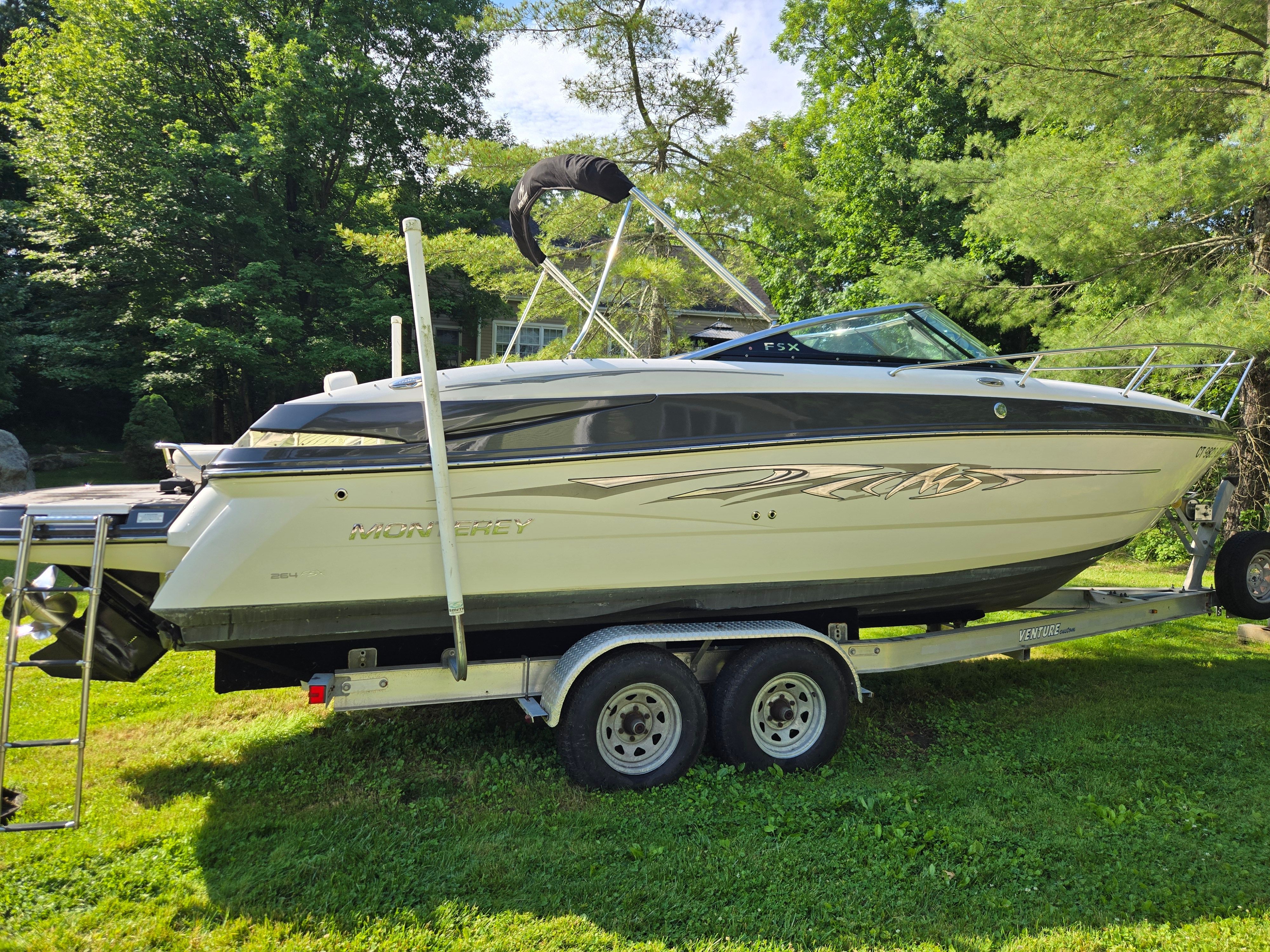 A 2013 Monterey 264 boat is on a trailer surrounded by greenery.